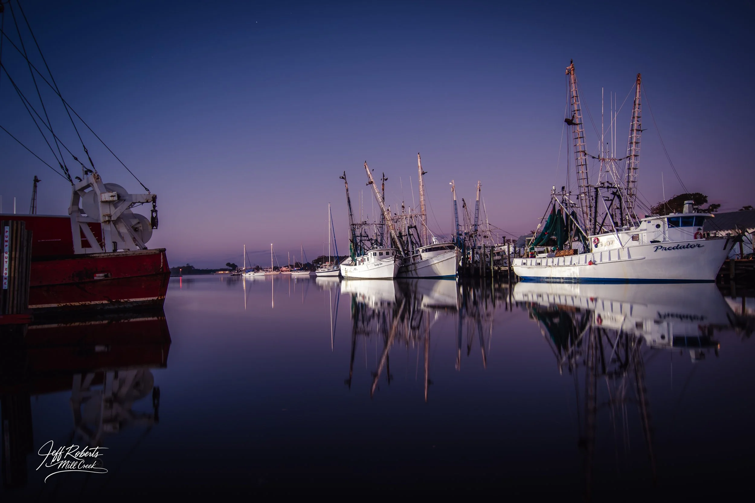 Boats docked at a serene marina during twilight with their reflections on calm water.