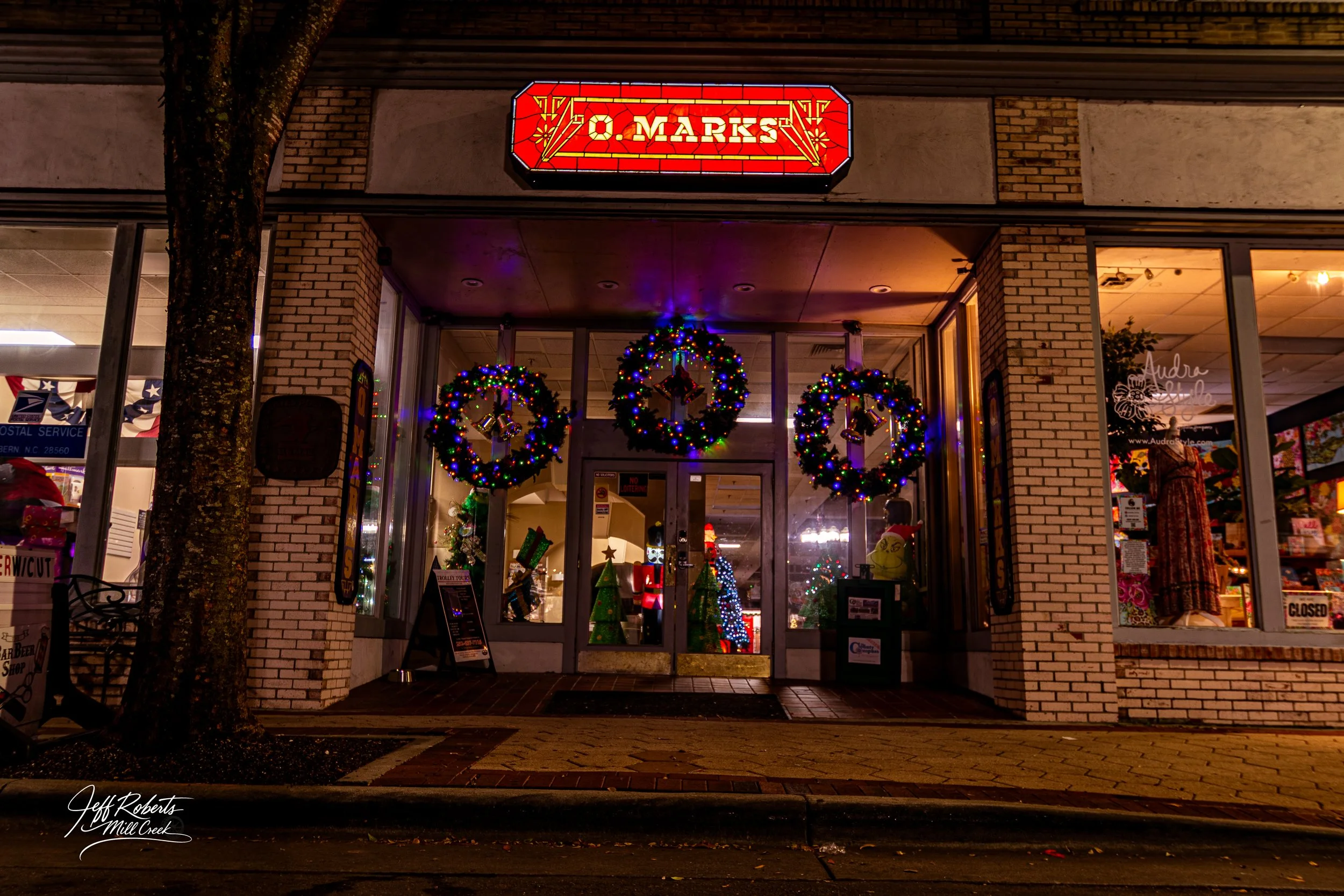  storefront decorated with Christmas wreaths and ornaments, illuminated Christmas trees inside, and a sign that reads 'O. MARKS'