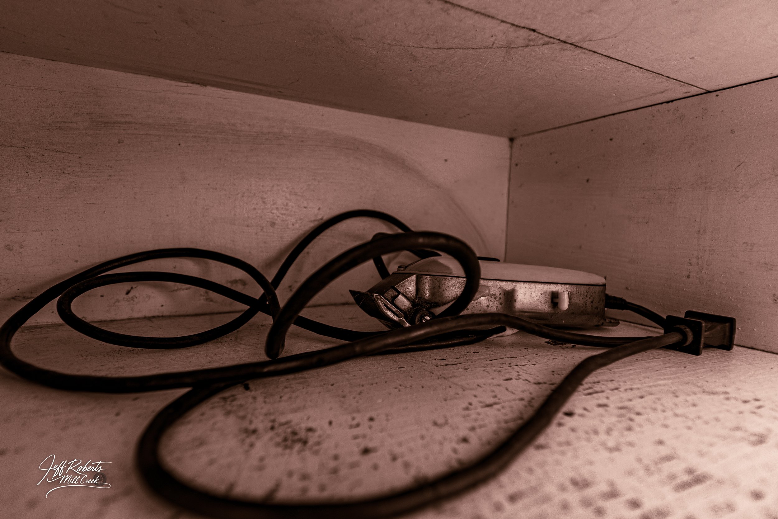 Electrical cords and a metal plug adapter lying on a dusty, white wooden shelf or cabinet floor.