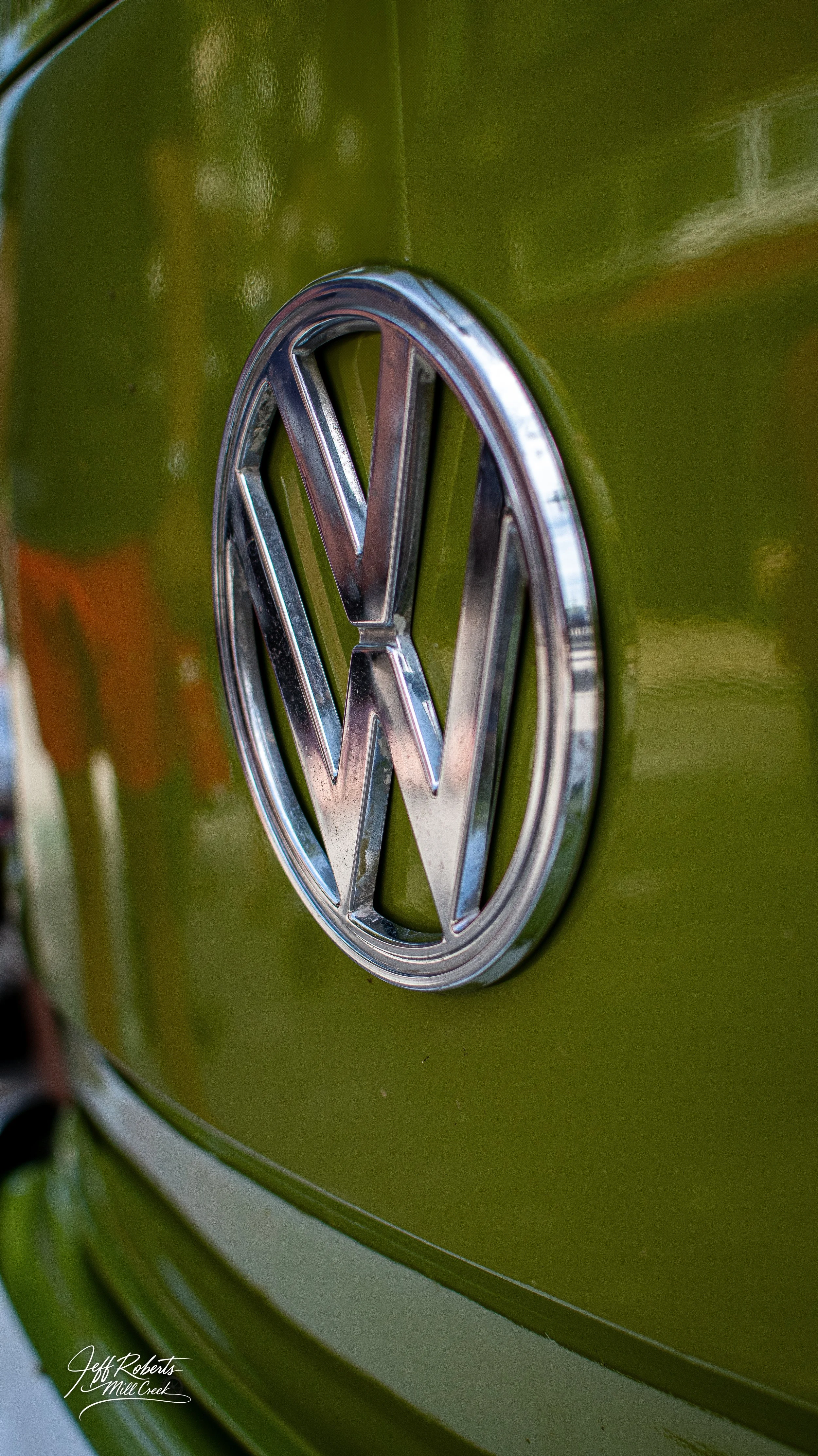 Close-up of a vintage Volkswagen logo on the front of a green vehicle.
