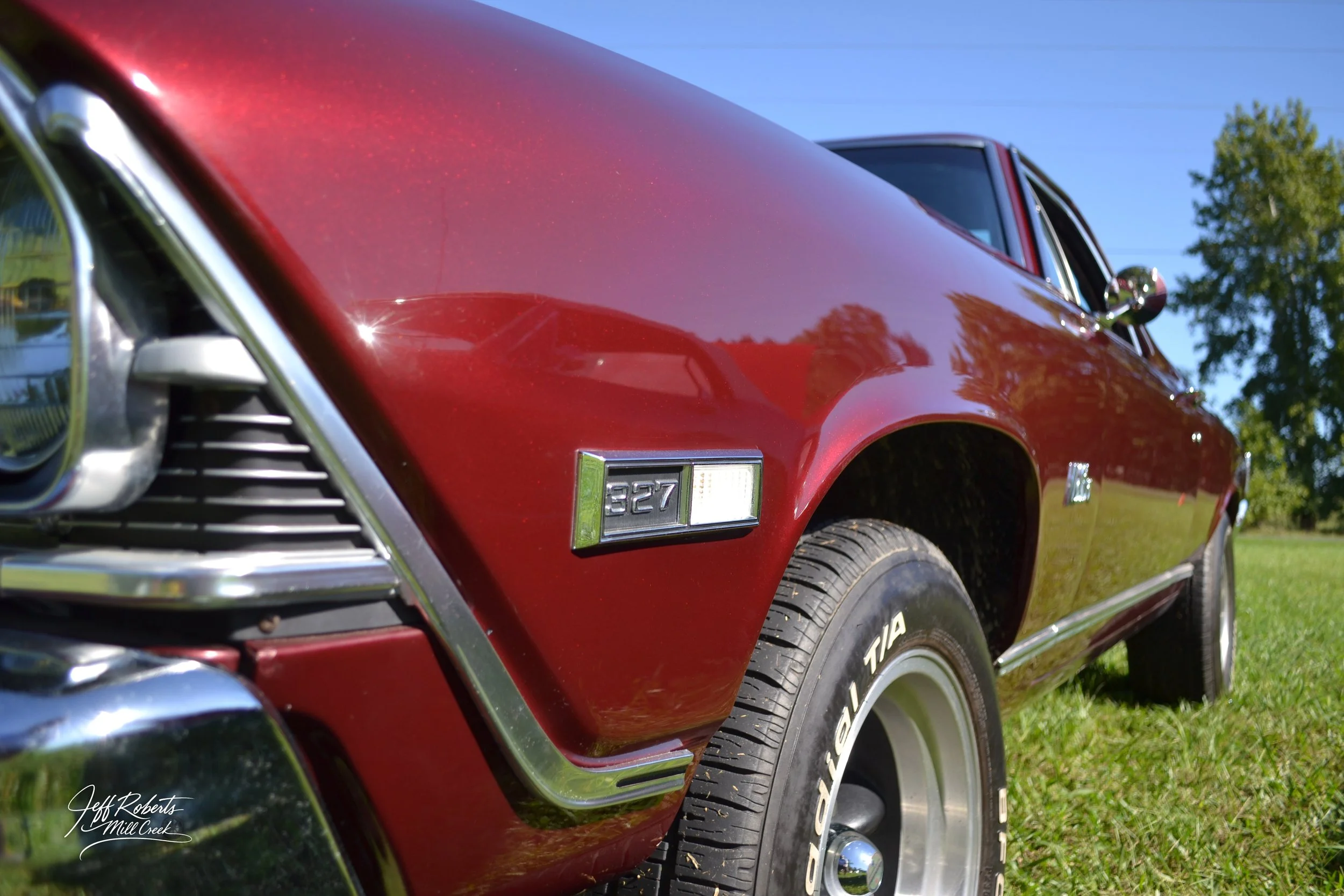 Close-up of a vintage red Chevrolet Camaro car showing the front left fender, wheel, and part of the hood with the emblem 327.