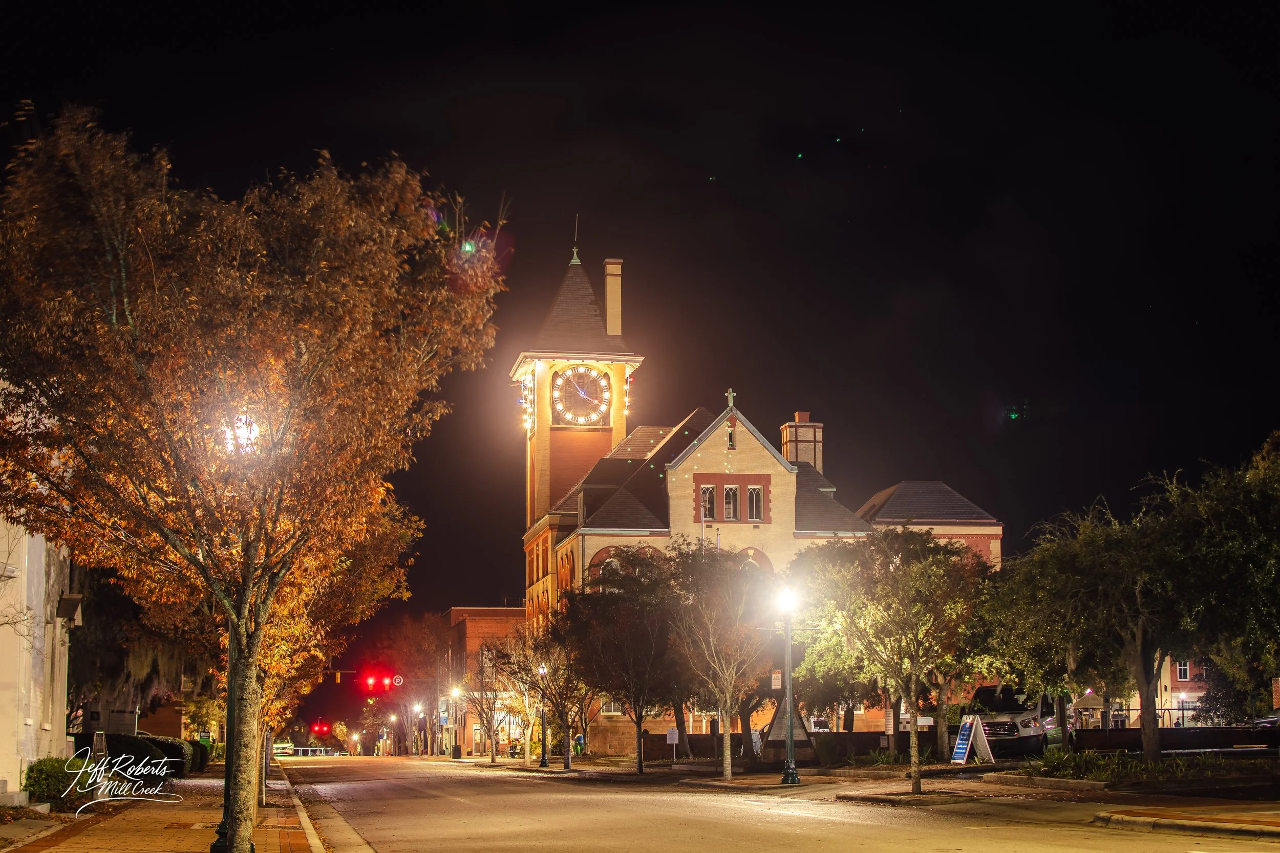 Night view of a small town with illuminated church and trees lining the street.