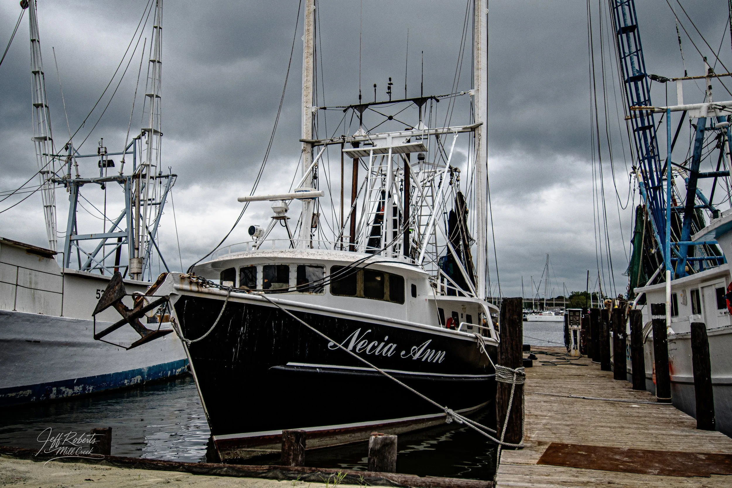 A boat named 'Necia Ann' docked at a marina with other boats, under dark cloudy skies.