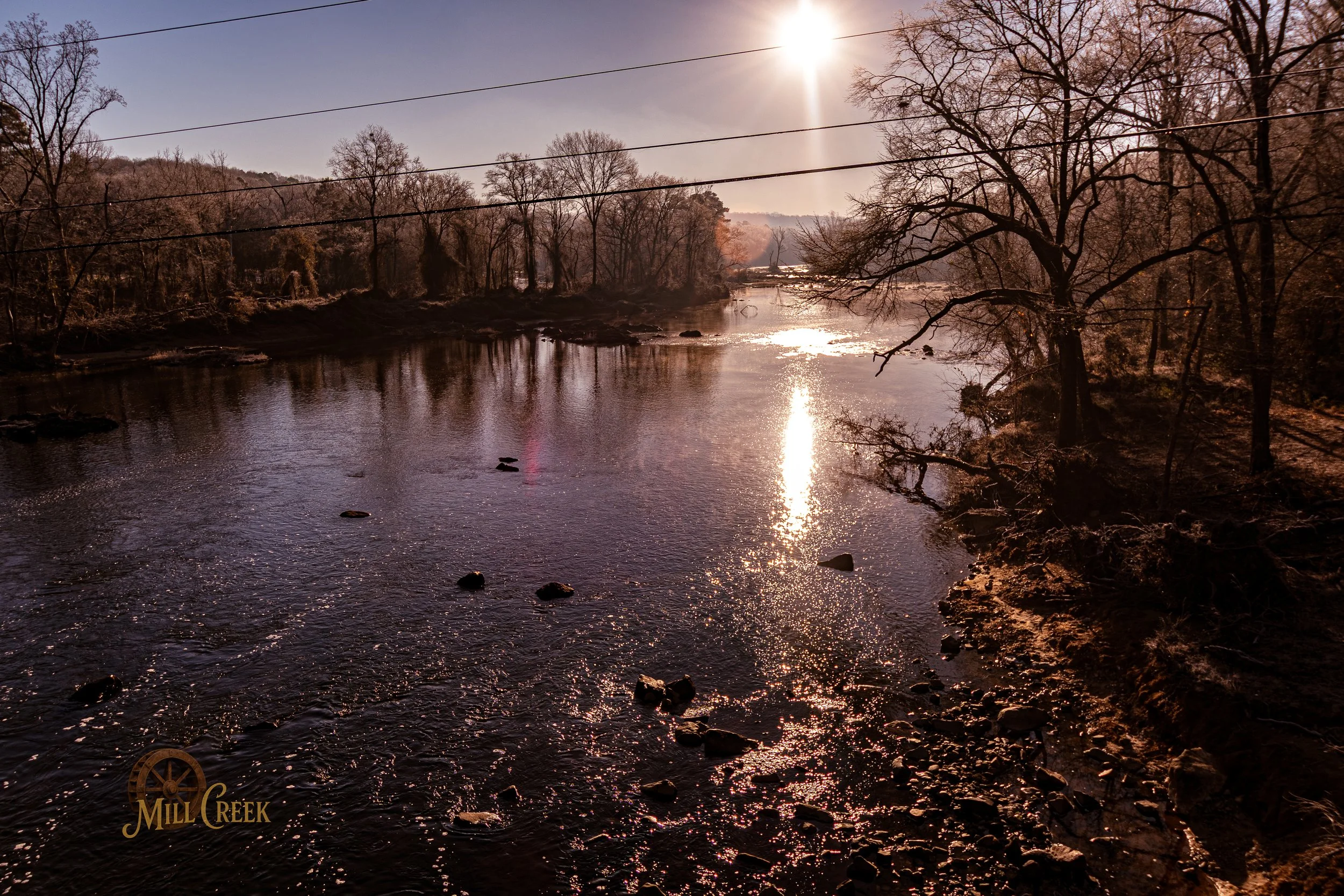 Sun setting over Mill Creek, with trees on the riverbank and a few power lines crossing the sky.