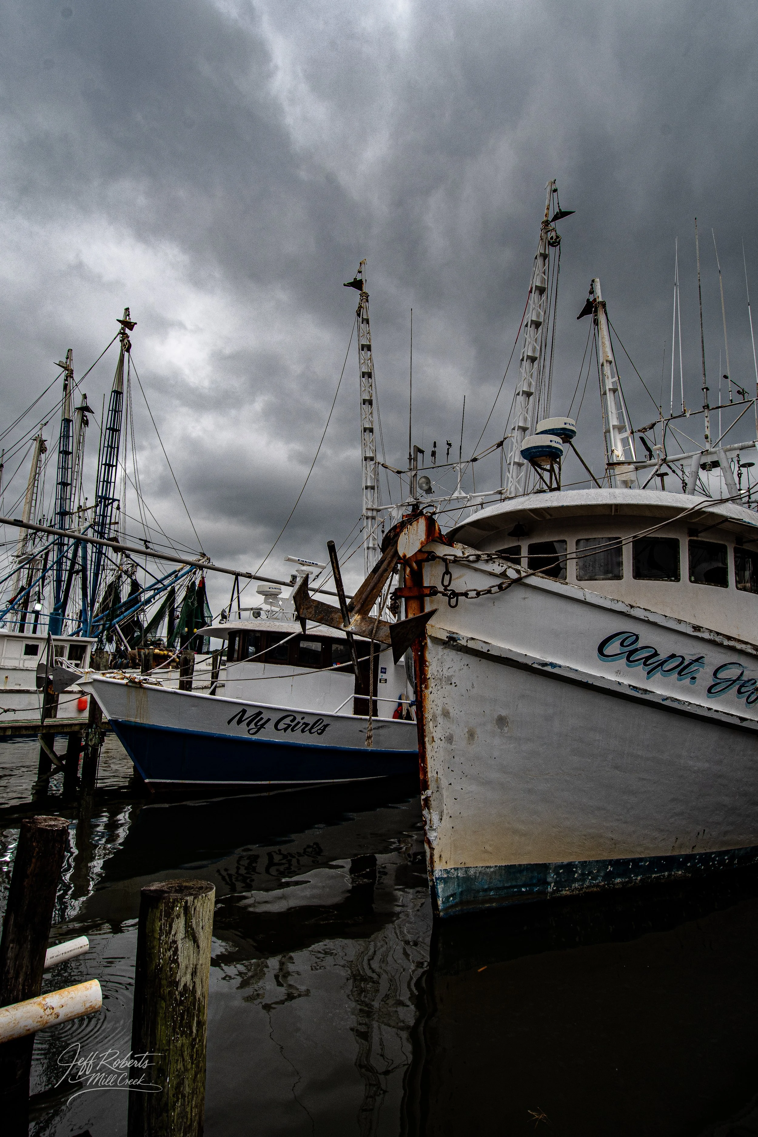 Several boats docked at a marina on a cloudy day, with dark stormy skies overhead.