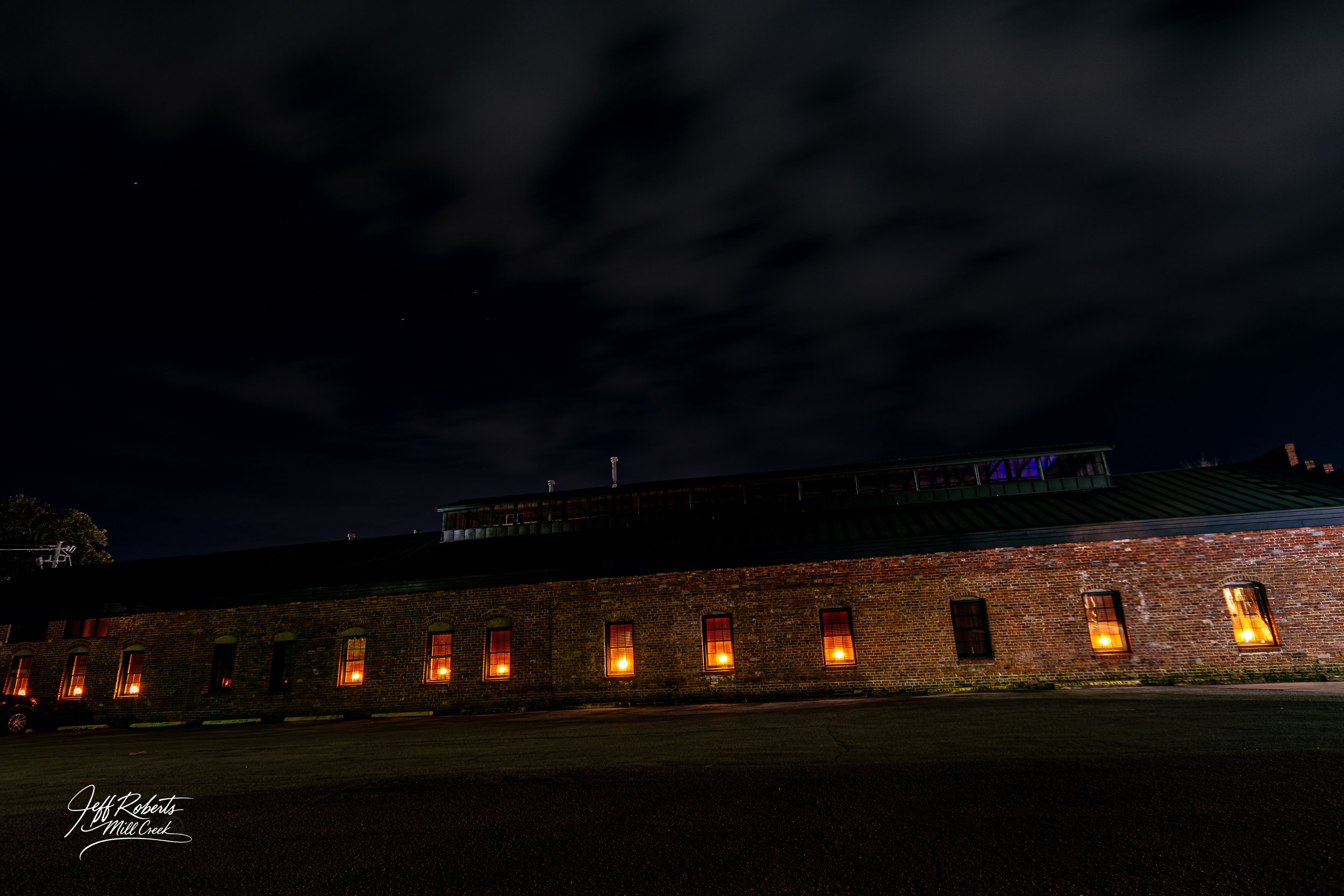Nighttime view of a brick building with several illuminated windows, under a dark, cloudy sky.