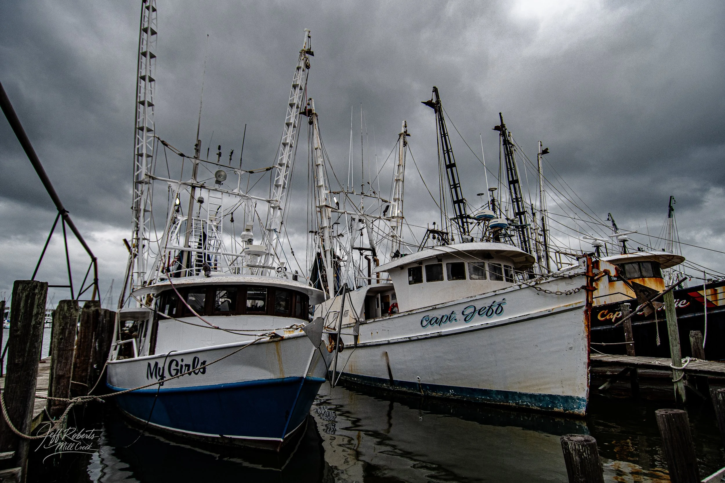 Two boats docked at a marina under a stormy sky, with the boat names 'My Girls' and 'Capt. Jeff' visible.