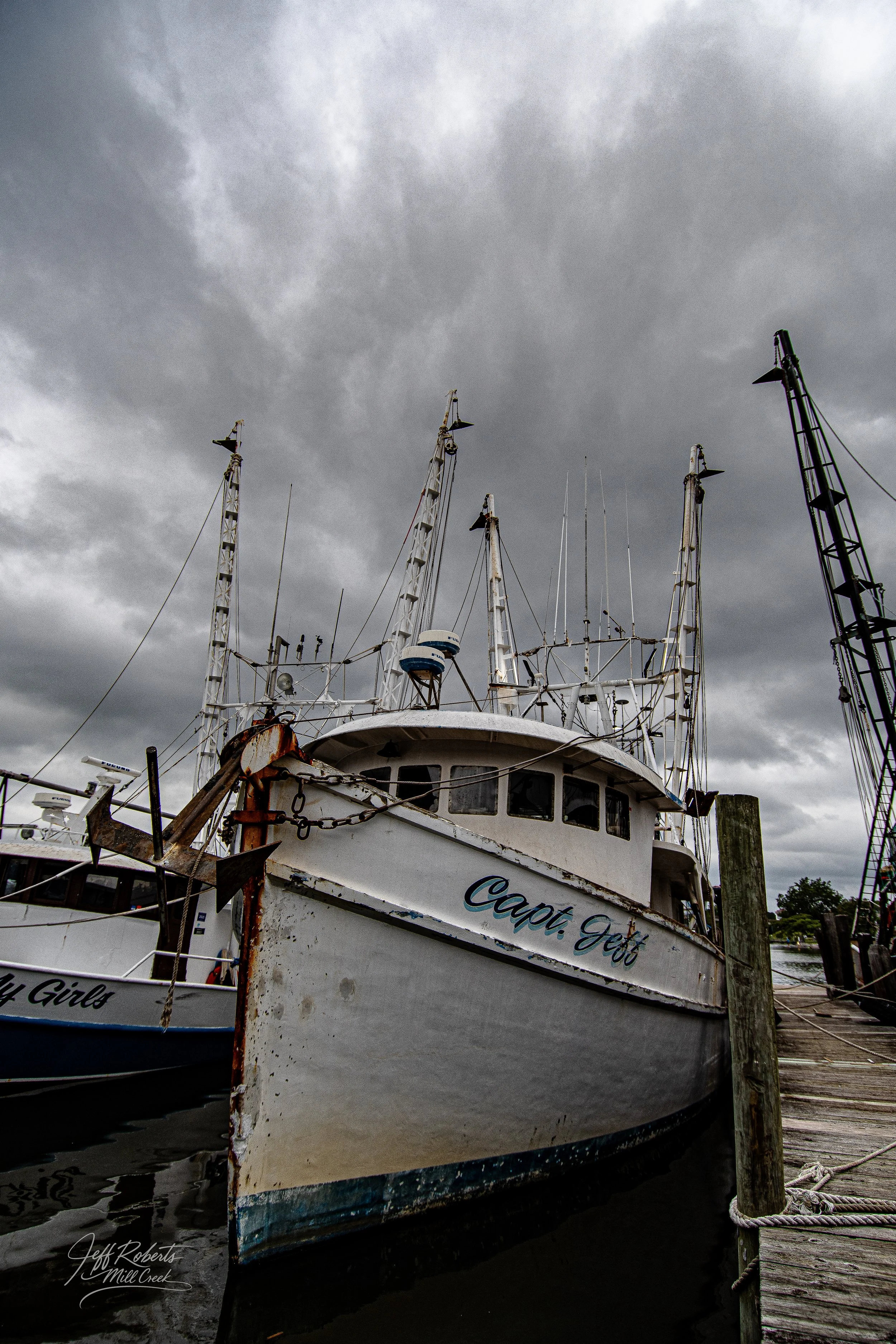 An old, rusted fishing boat named 'Capt. Jeff' docked at a pier under dark, cloudy skies.