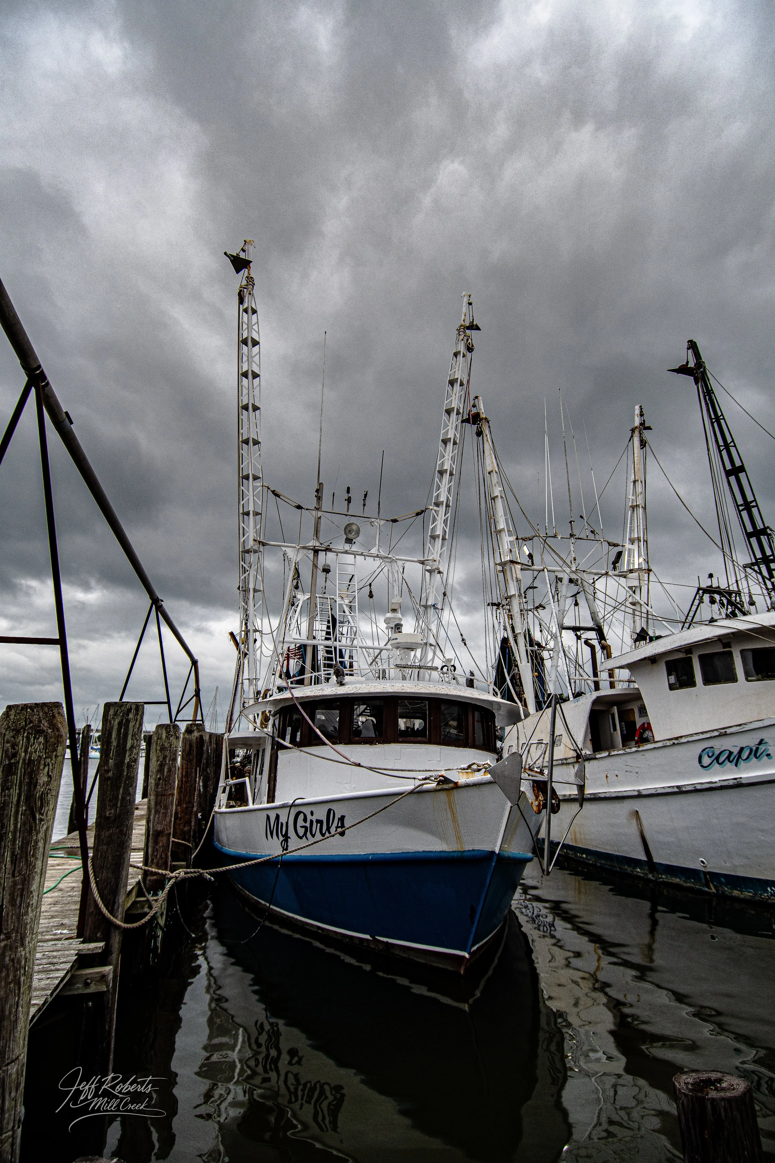 A marina with two boats docked, one named 'My Girl' and the other partially visible, under a dark, cloudy sky.