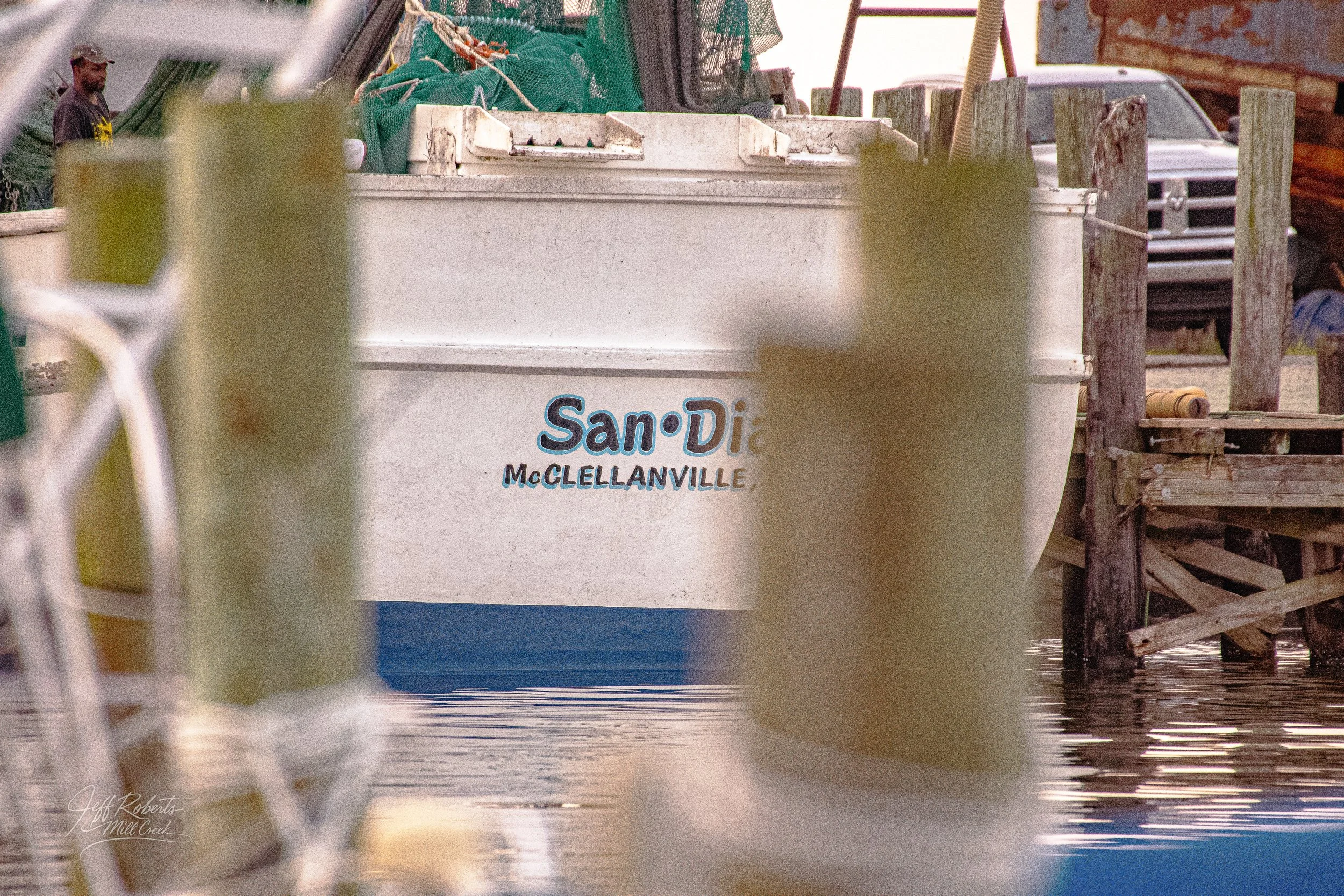Close-up view of a boat with the text "San Diego McLellanville" on its side, seen through a blurry foreground of yellow cylindrical objects.
