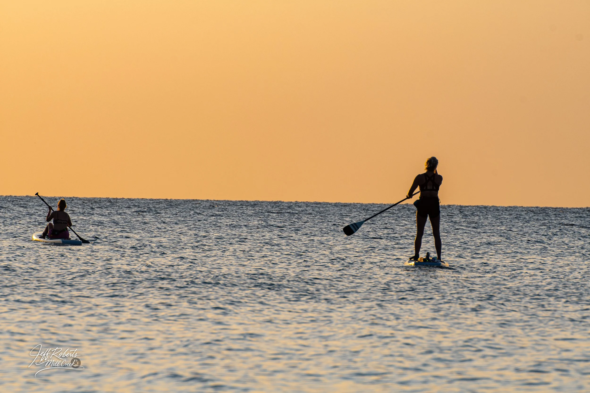 Silhouettes of two people paddleboarding on the water during sunset