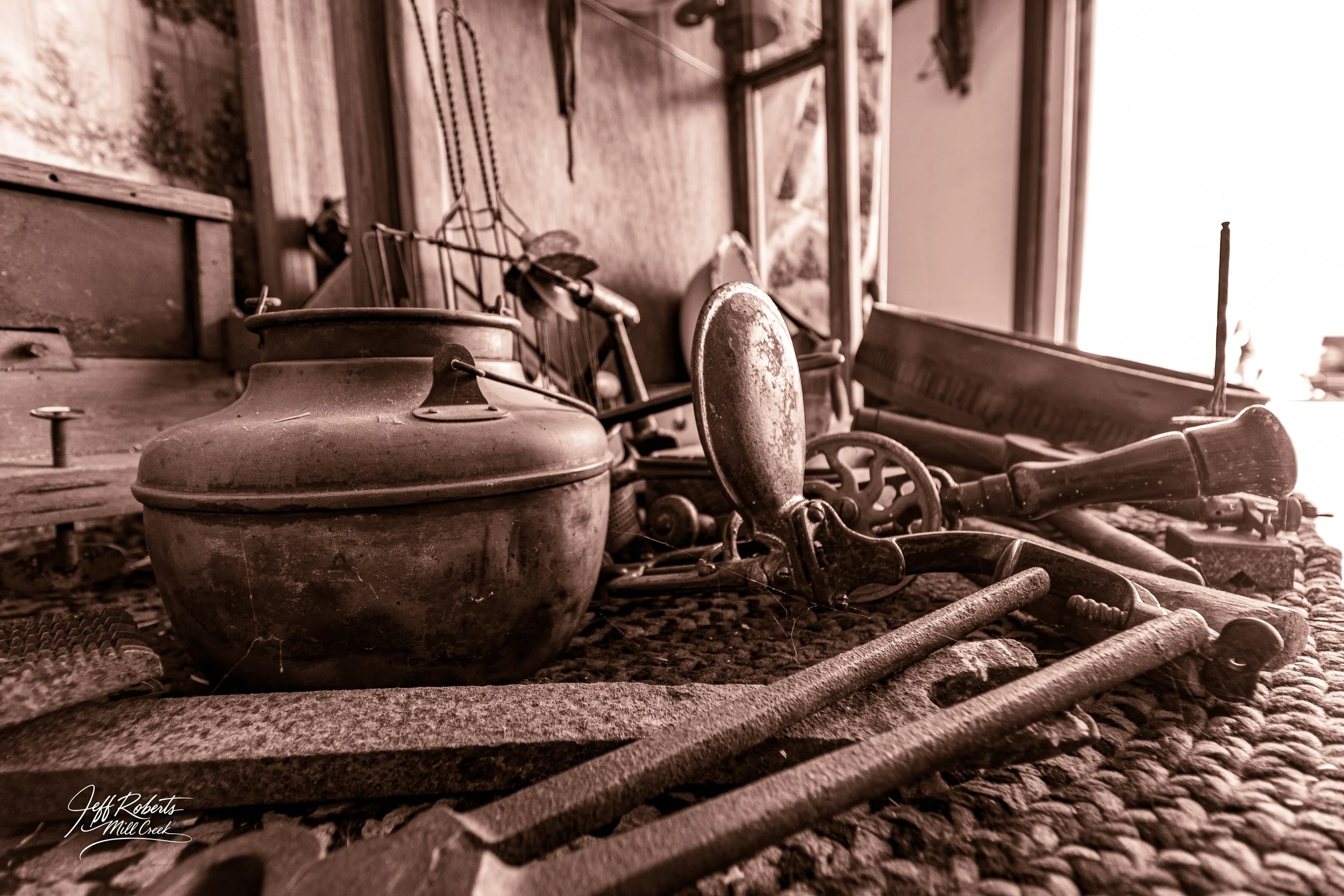 Old vintage tools and objects including a metal kettle, hand saws, and other rusty tools on a workbench in a workshop or shed.