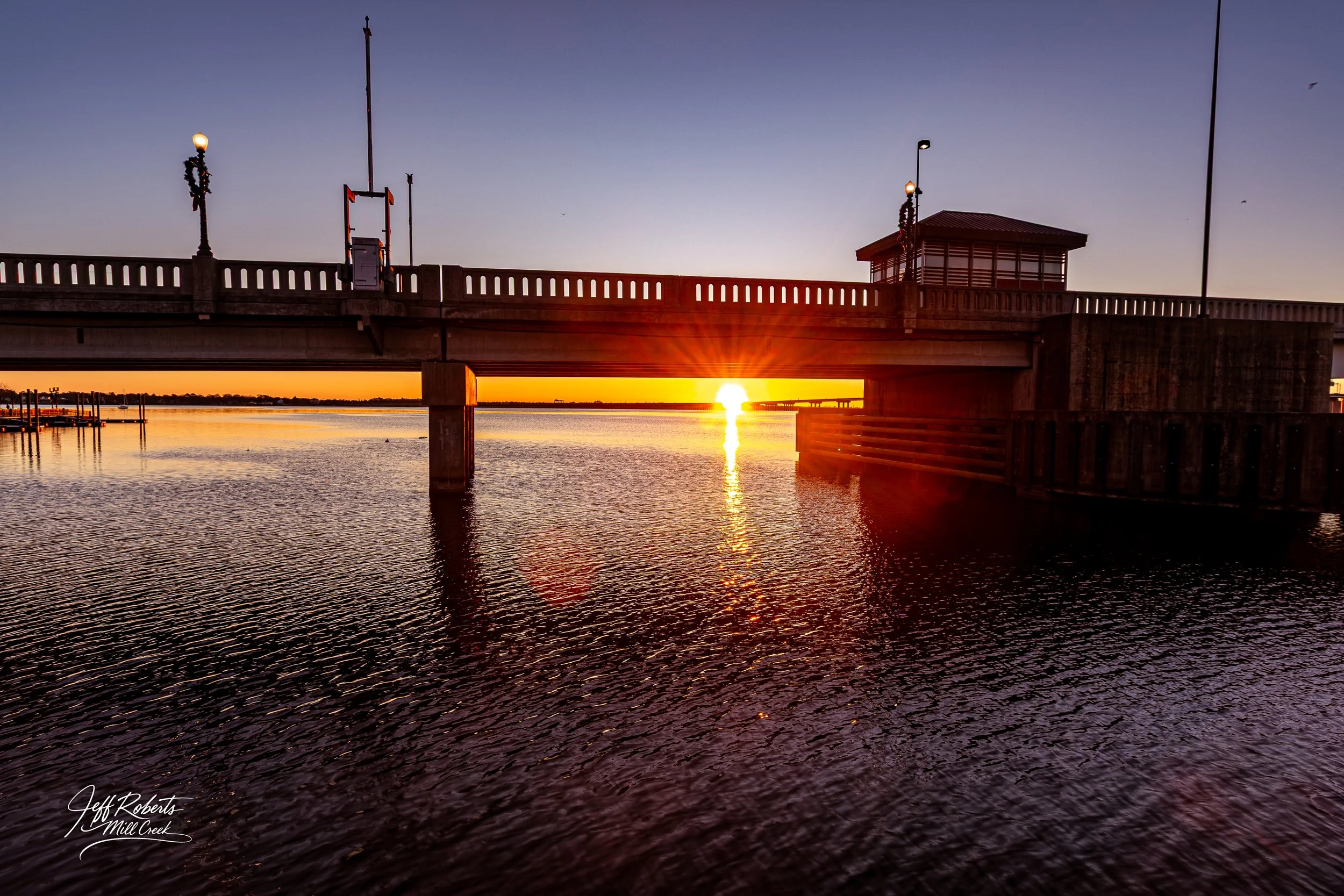 Sunset over a pier extending into the water, with the sun setting behind the horizon and casting a glow on the water.