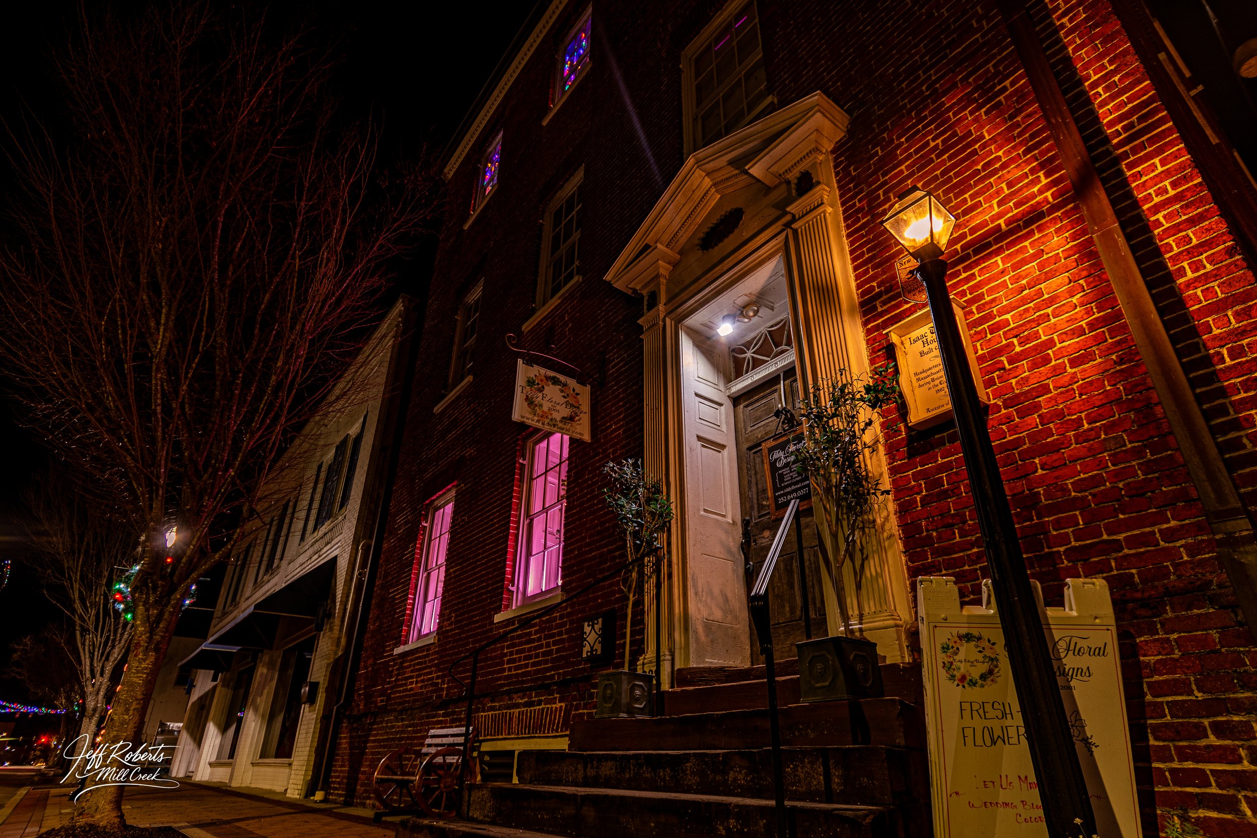 Nighttime street view of a brick building with decorated windows, illuminated entrance, and a streetlamp.