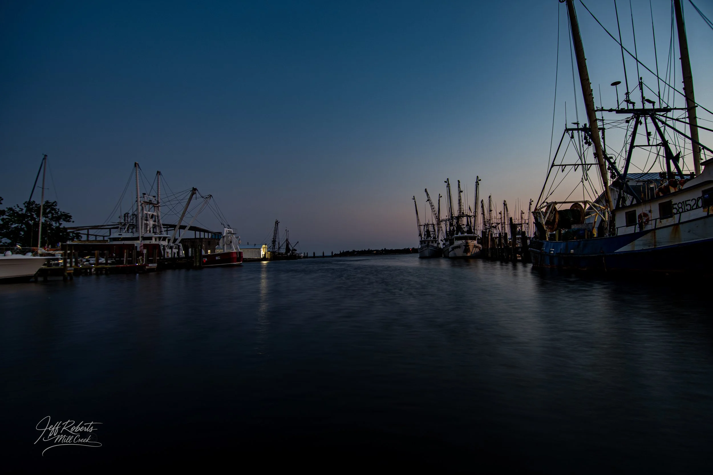 Boats docked at a harbor during dusk, with calm water reflecting the darkening sky.