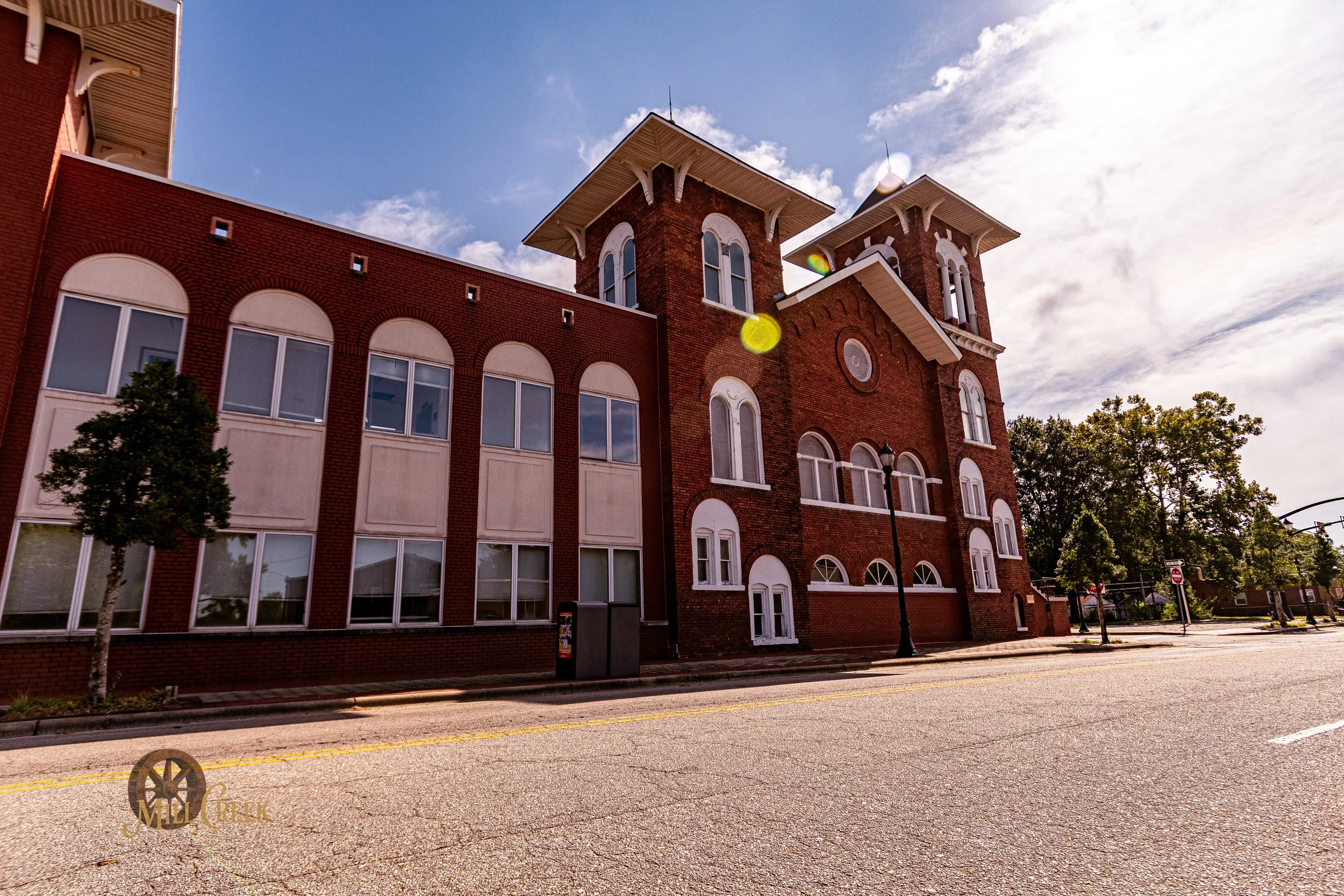 A historic brick building with arched windows and towers, set against a partly cloudy sky on a quiet street.