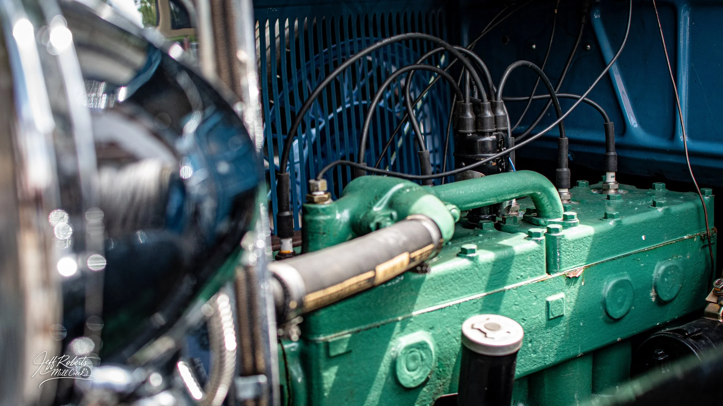 Close-up view of a vintage car engine with green-painted components, black wires, and metallic parts, inside the engine bay.