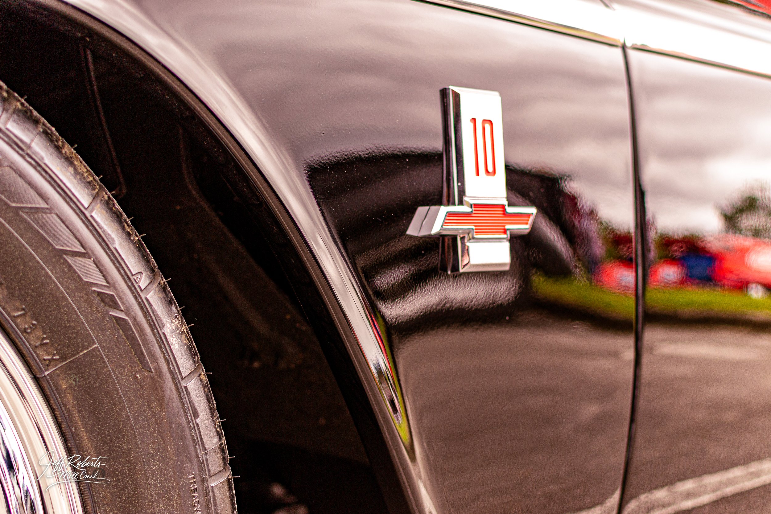 Close-up of a vintage black car's rear fender with a 10 Chevrolet badge and a portion of the tire visible.