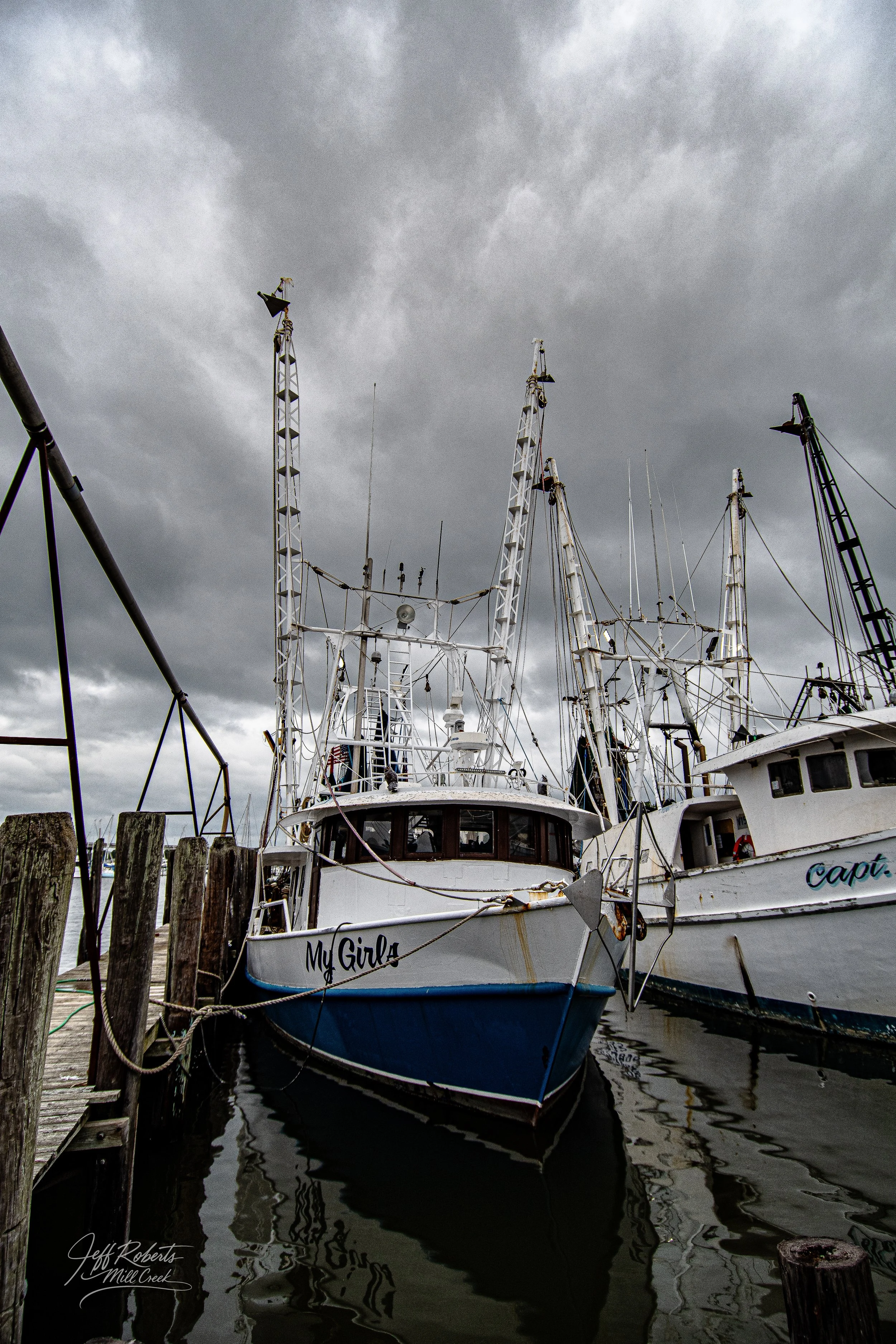 A docked boat named 'My Girls' at a marina under dark, cloudy skies.