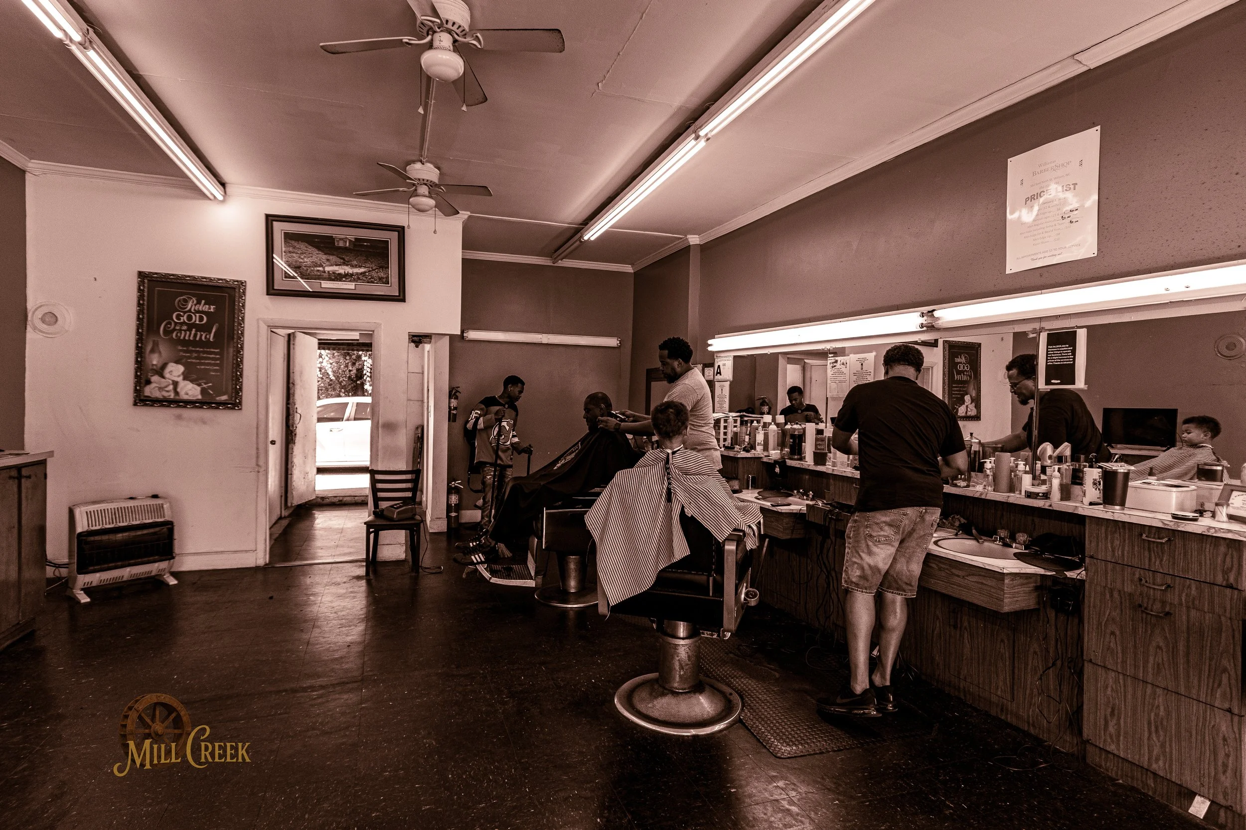 Interior of a barbershop with customers receiving haircuts and barbers working behind the counter.