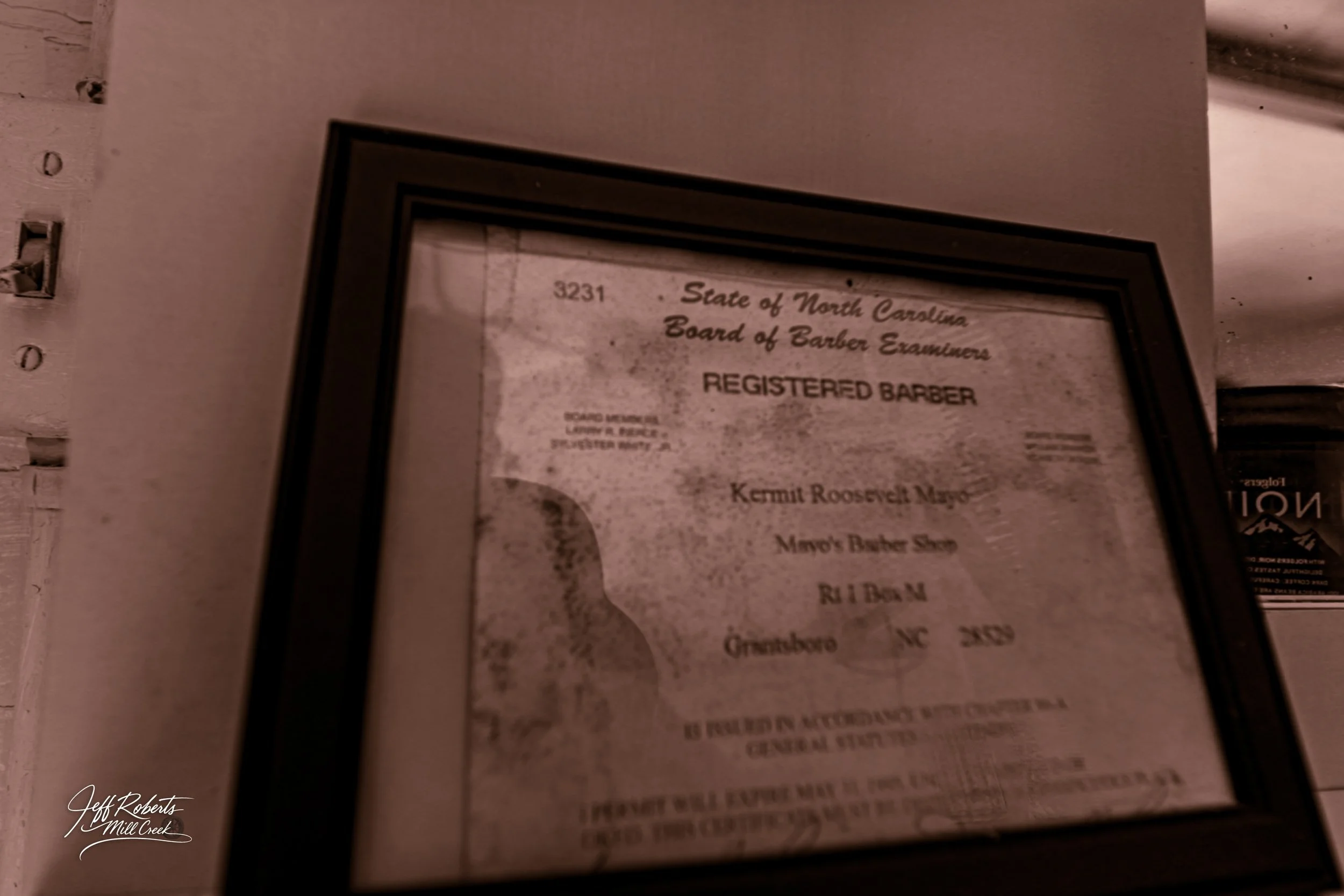 Framed certificate from the North Carolina Board of Barber Examiners recognizing Kermit Roosevelt for completing barber training at Mayor's Barber Shop in Greensboro, North Carolina.