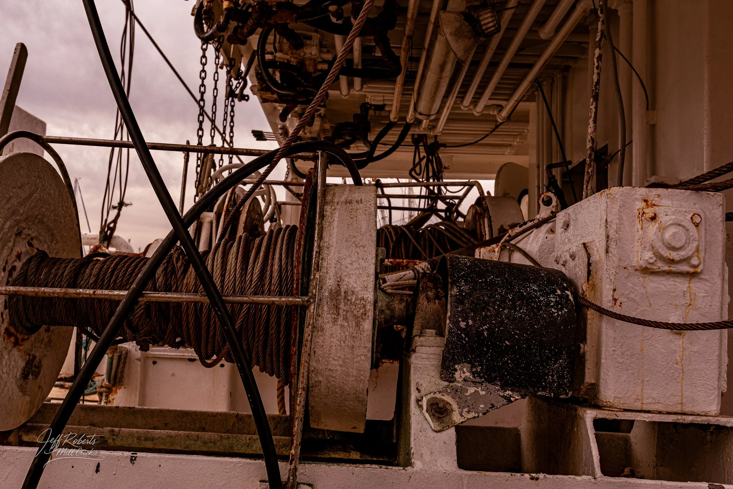 Close-up of weathered ship winch and pulley system with rusty and worn metal components, cables, and ropes on a boat deck.