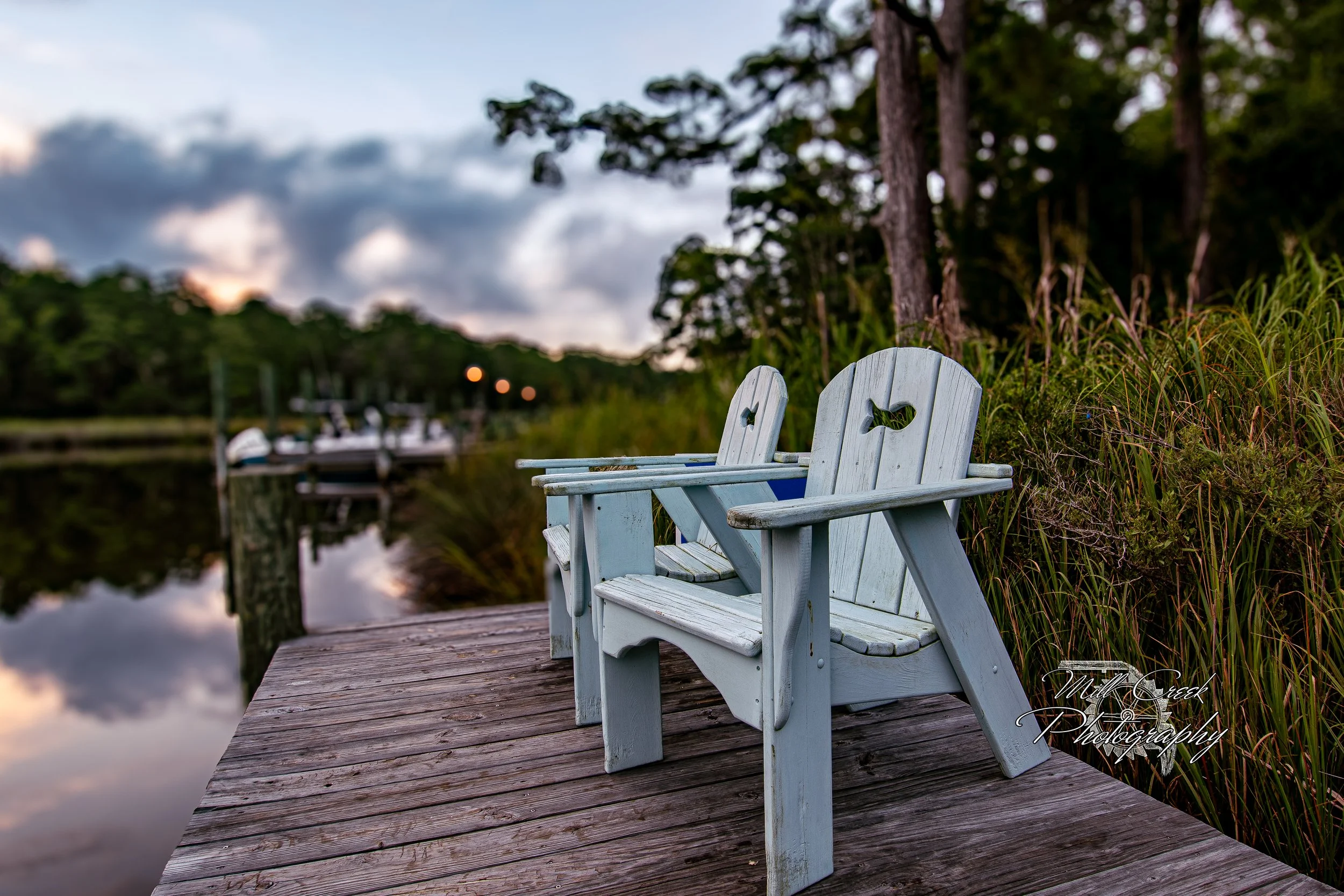 "Adirondacks at Ease"
Two seaside chairs wait on a quiet dock, perfectly placed for sunset watching. A soft blur of creek and pines sets a dreamy, coastal backdrop.