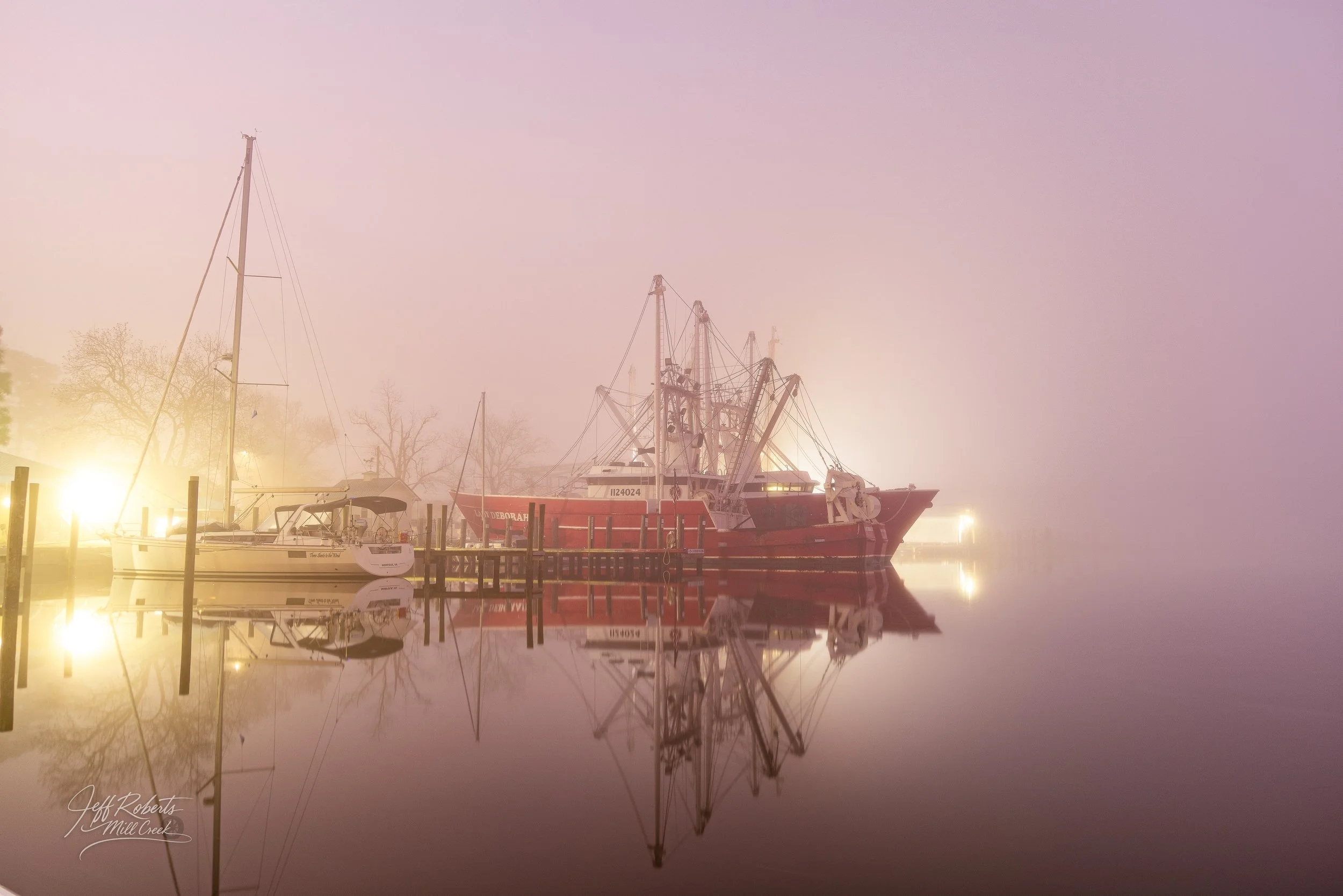 Boats docked at a foggy marina, reflecting on calm water