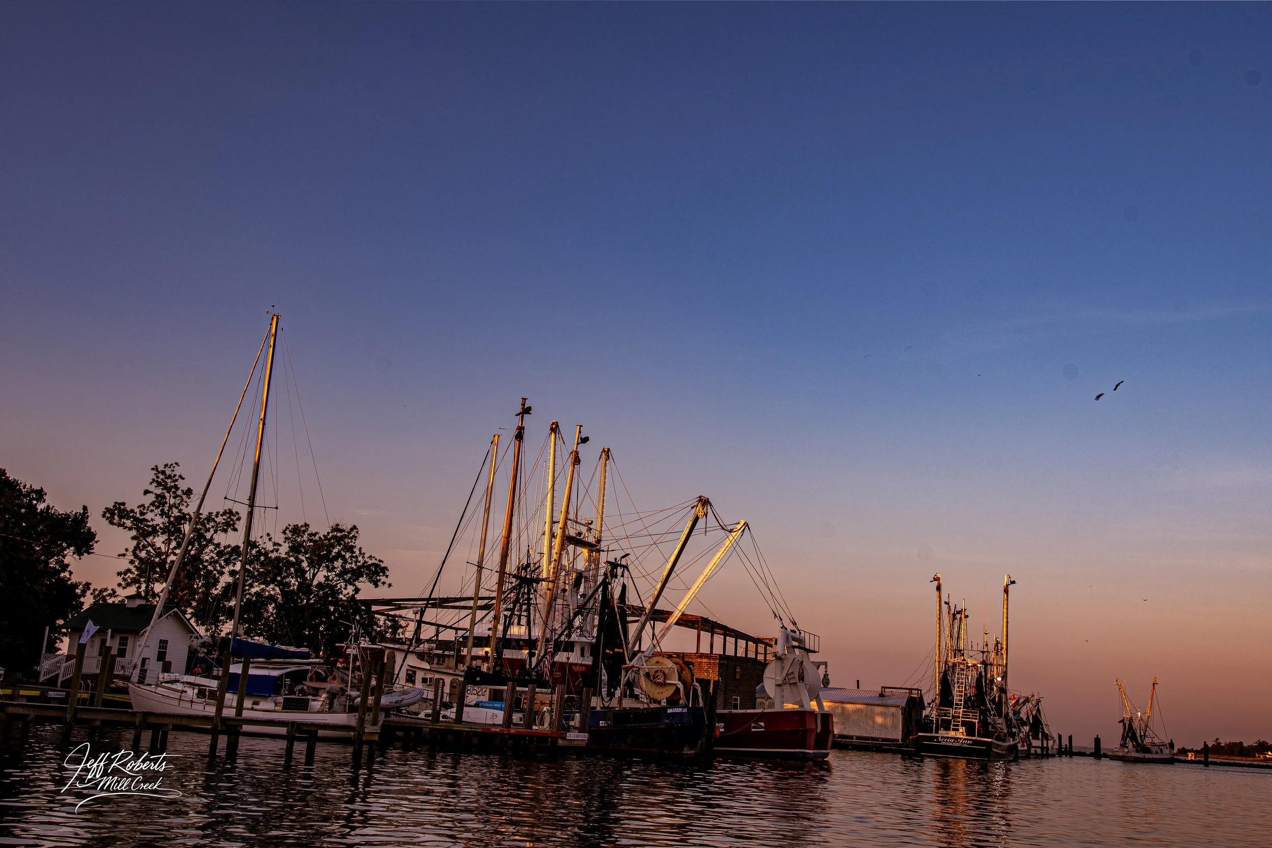 Boats docked at a marina during sunset with a colorful sky and reflections on the water.