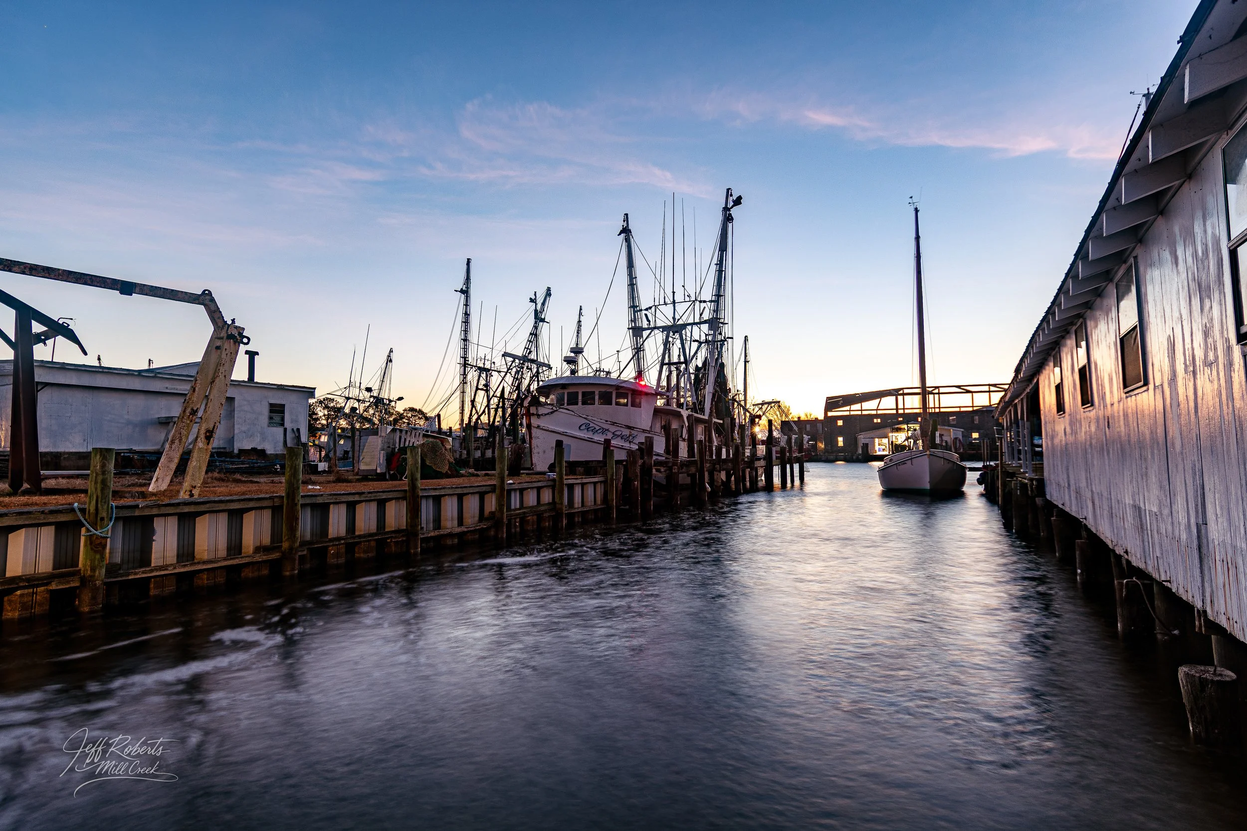 Boat dock with anchored boats along a wooden pier at sunset.
