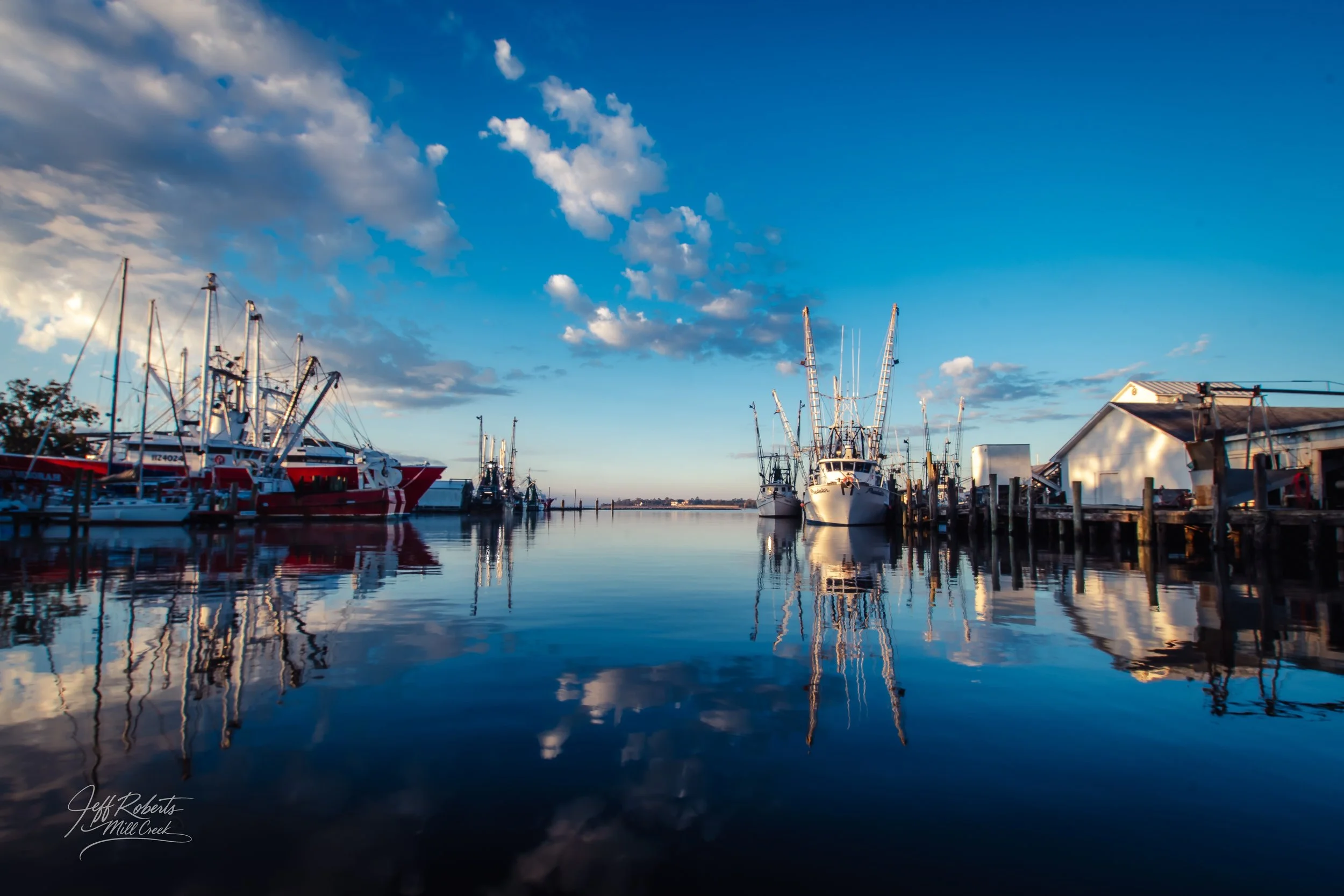 Boats docked at a marina during sunset with a partly cloudy sky and reflections in the water.