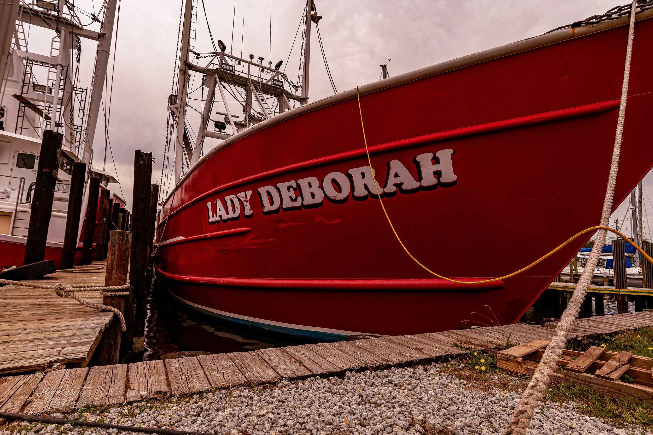 Red boat named Lady Deborahh docked at a marina spurred by wooden pier and other boats.