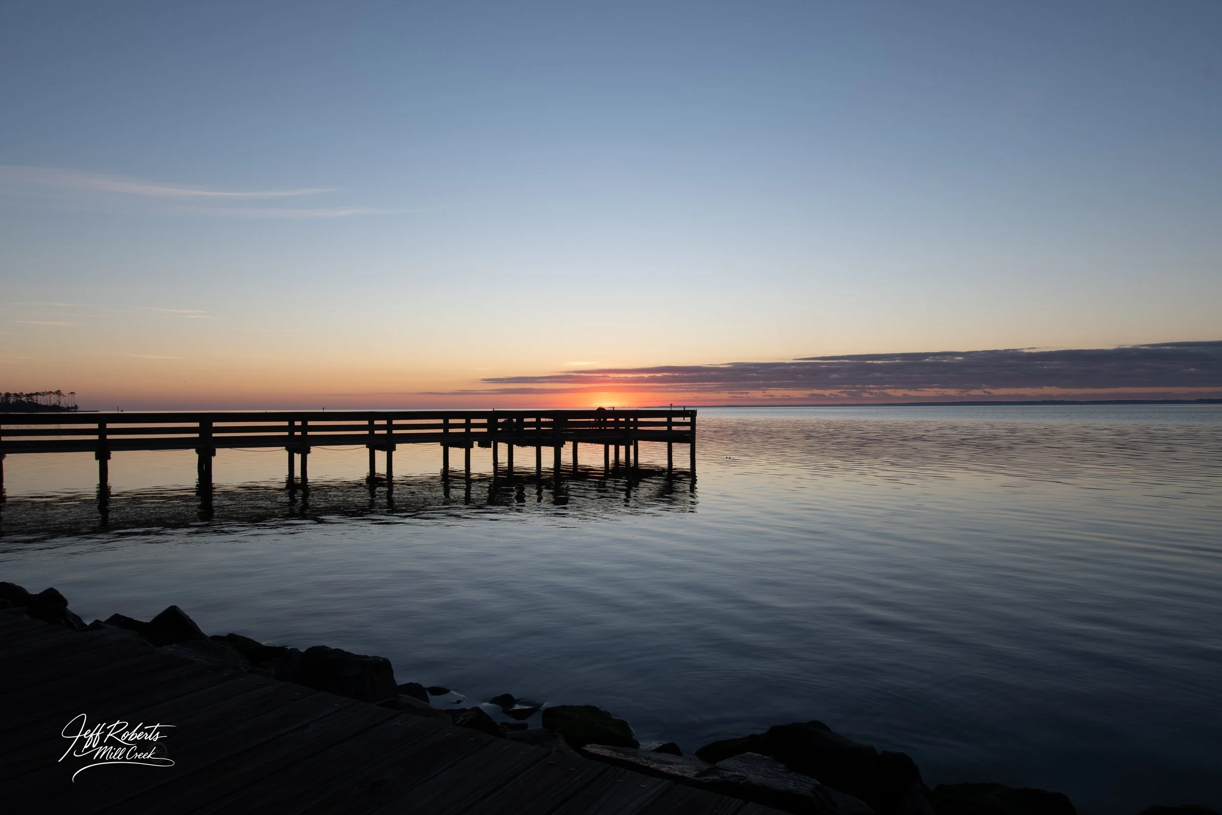 Sunset over a calm body of water with a wooden pier extending into the water.