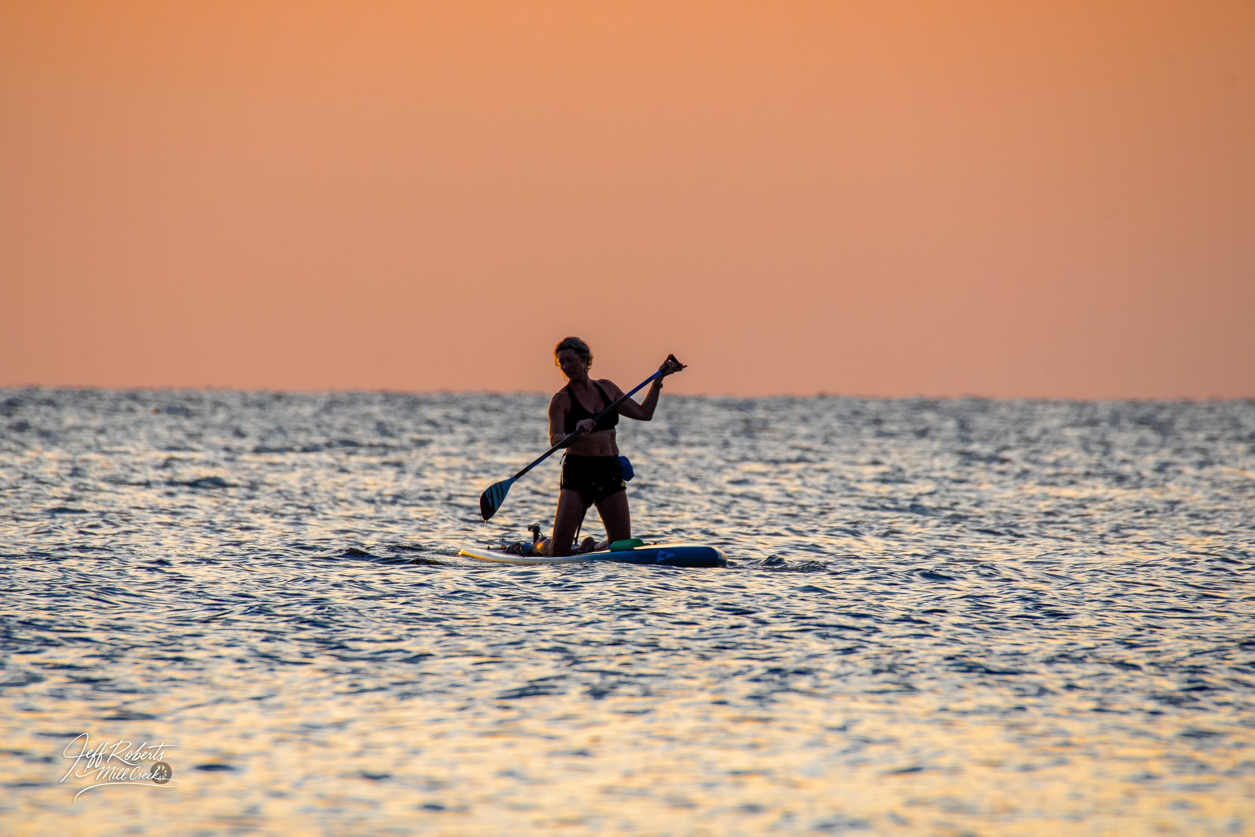A person paddleboarding on the water during sunset
