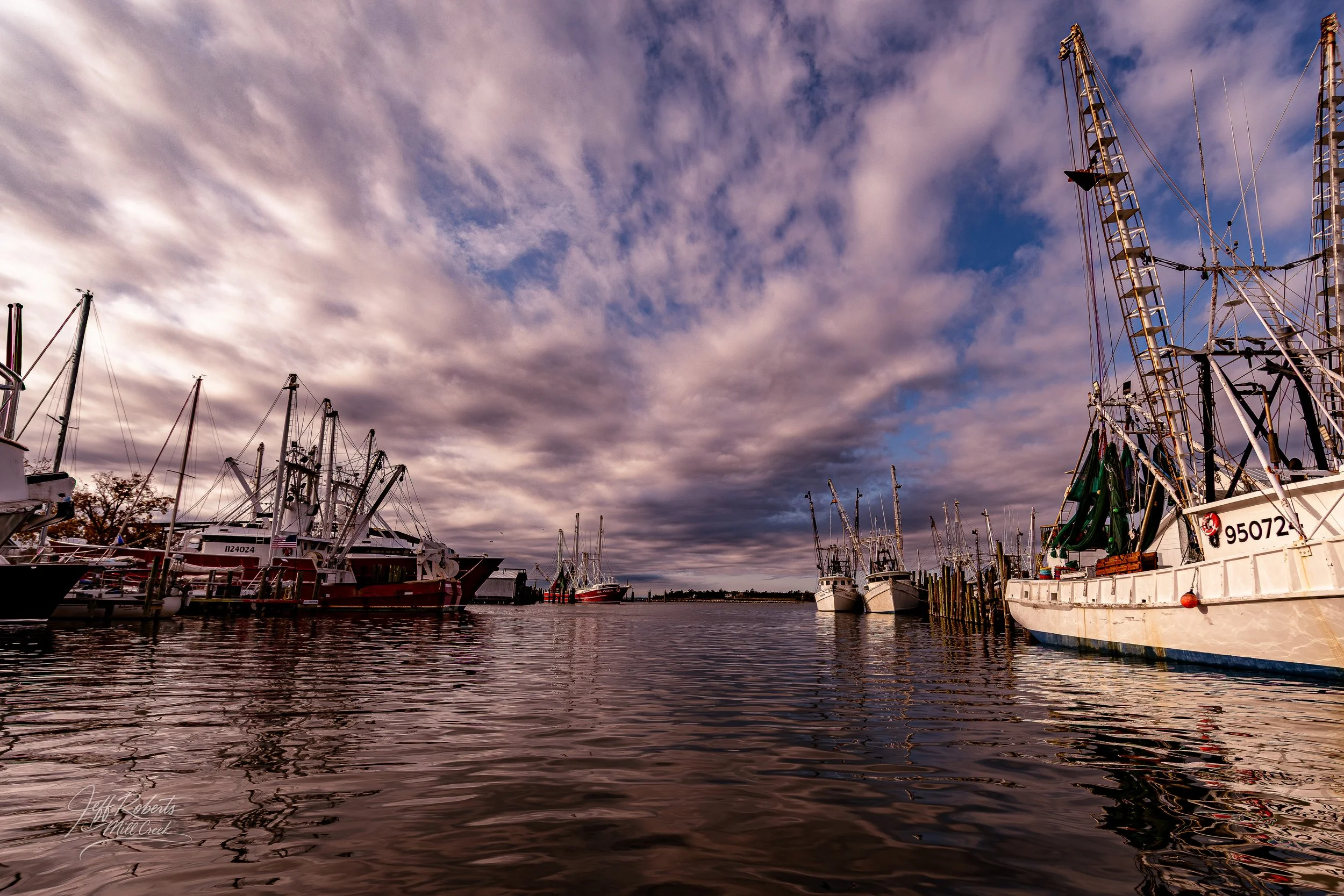 A harbor with boats docked along the water, under a cloudy sky during sunset or sunrise.