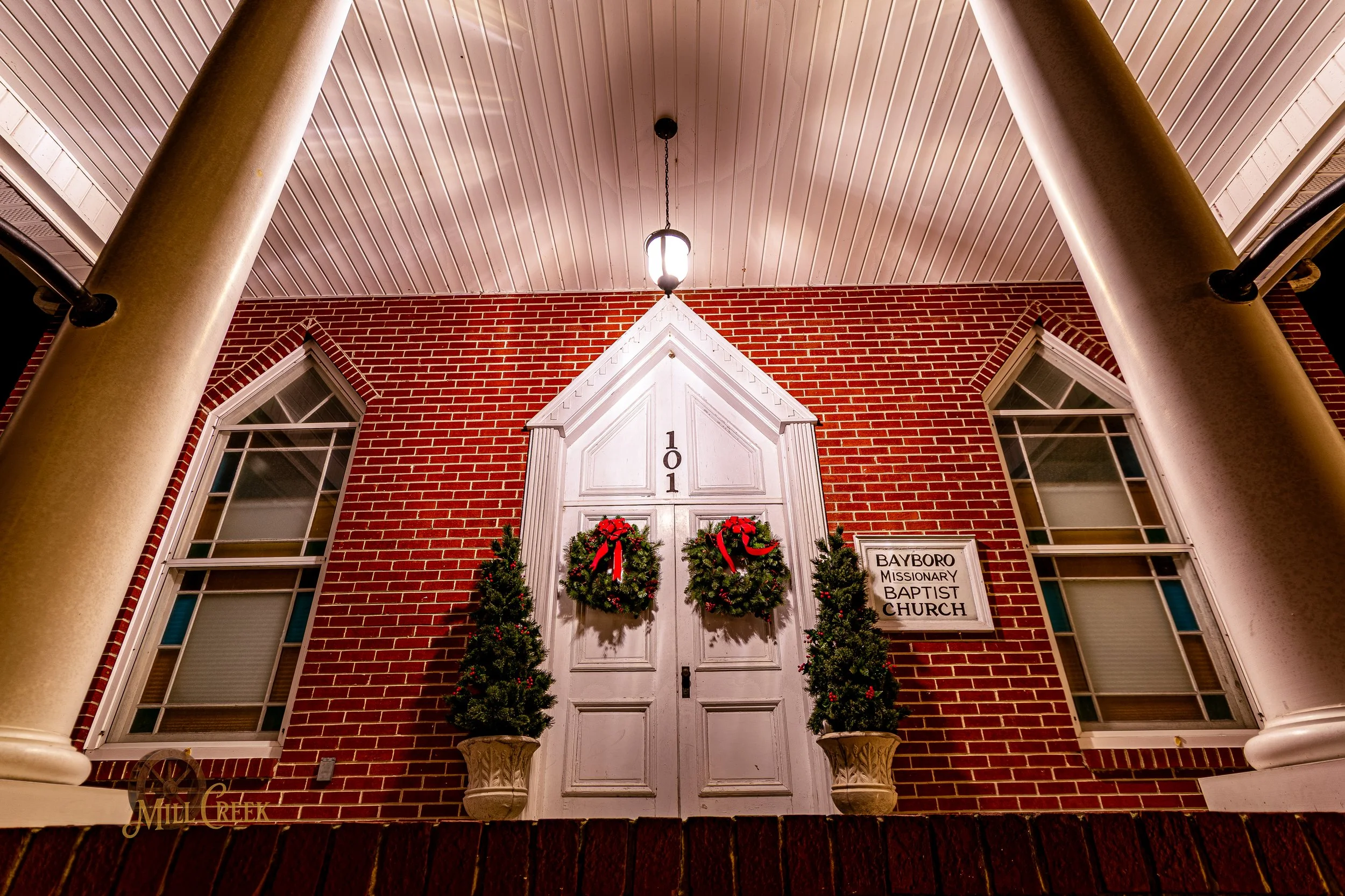 Front porch of Baybore Missionary Baptist Church decorated with Christmas wreaths and potted Evergreens.