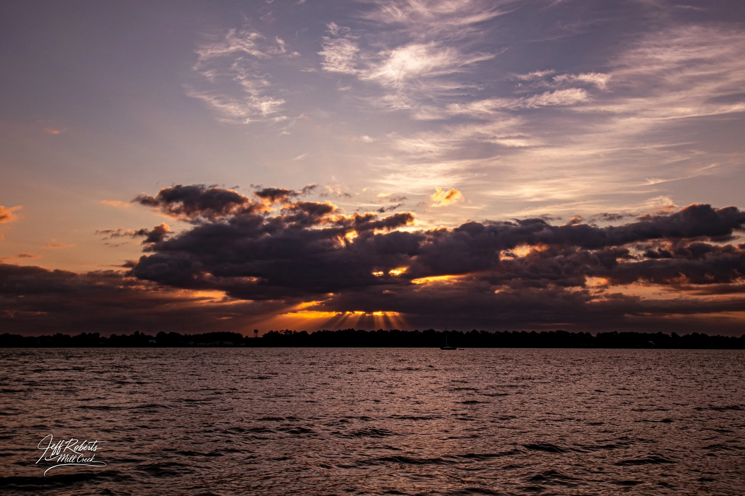 A sunset over a body of water with clouds in the sky and a distant shoreline.