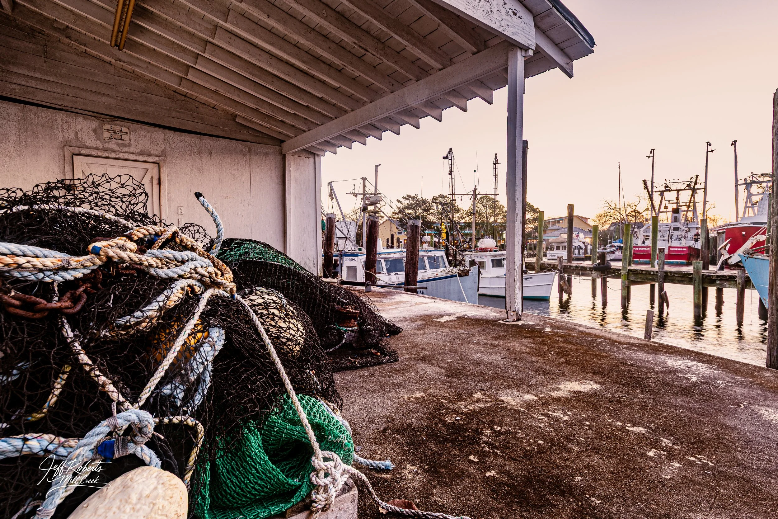 Fishing boats docked at a marina during sunset with fishing nets and ropes in the foreground