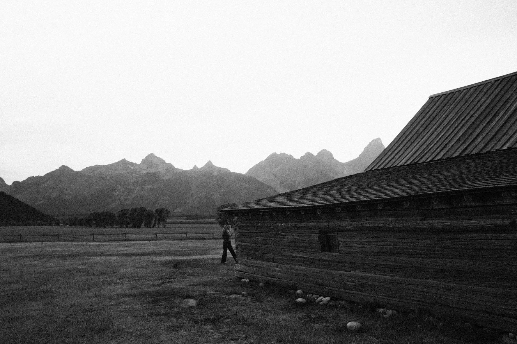 Black and white photograph of an old pioneer barn with mountain peaks in the background, reflecting intentional living and quiet exploration.