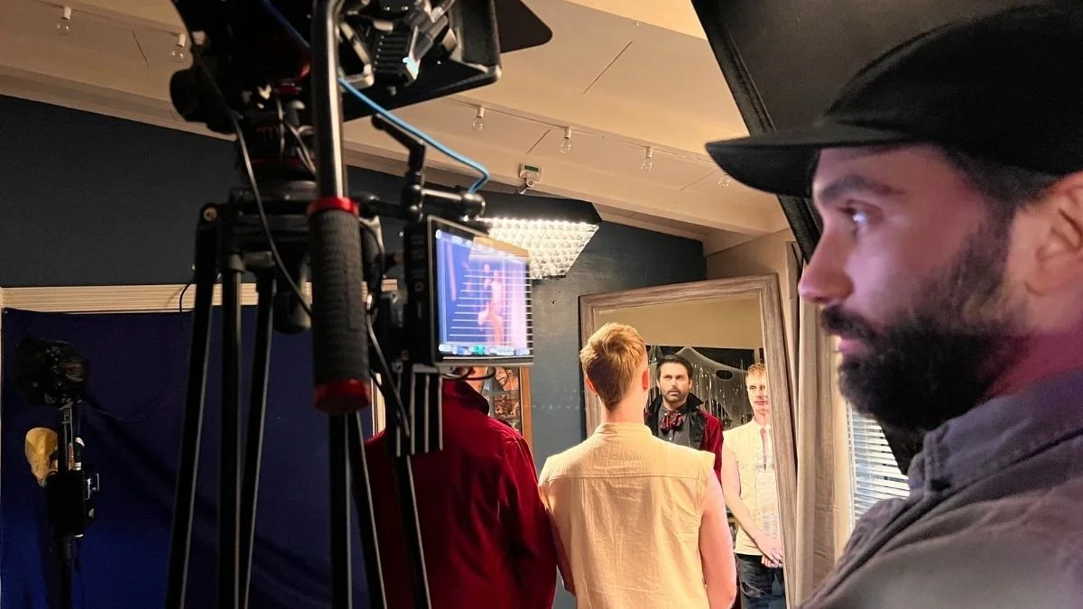 Behind the scenes of a photoshoot showing a cameraman filming a model in front of a mirror with two other people observing.