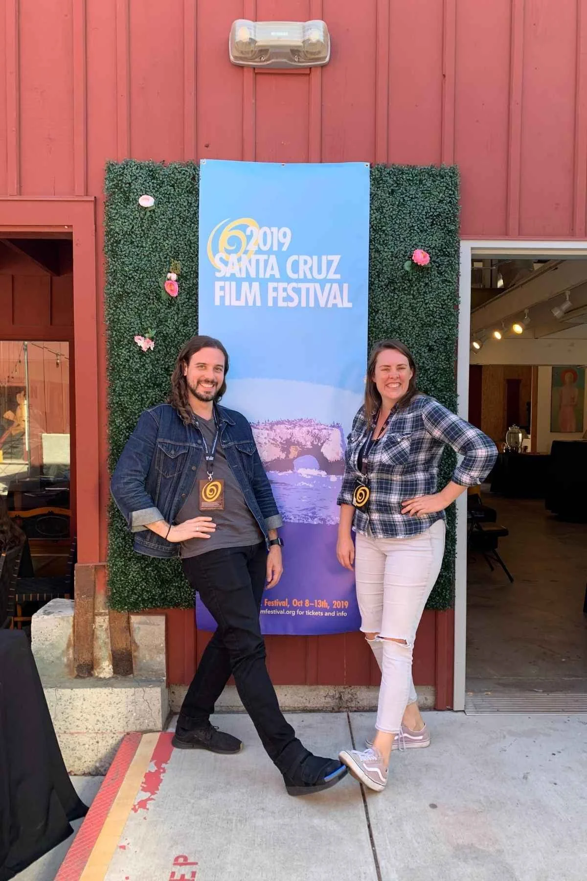 Two people smiling in front of a Santa Cruz Film Festival banner at an outdoor event.