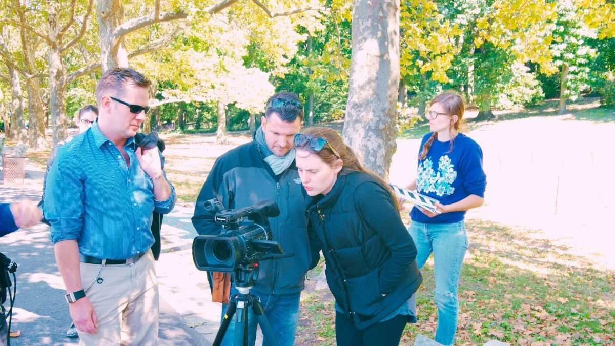Group of people working with a camera outdoors in a park, surrounded by trees and sunlight.