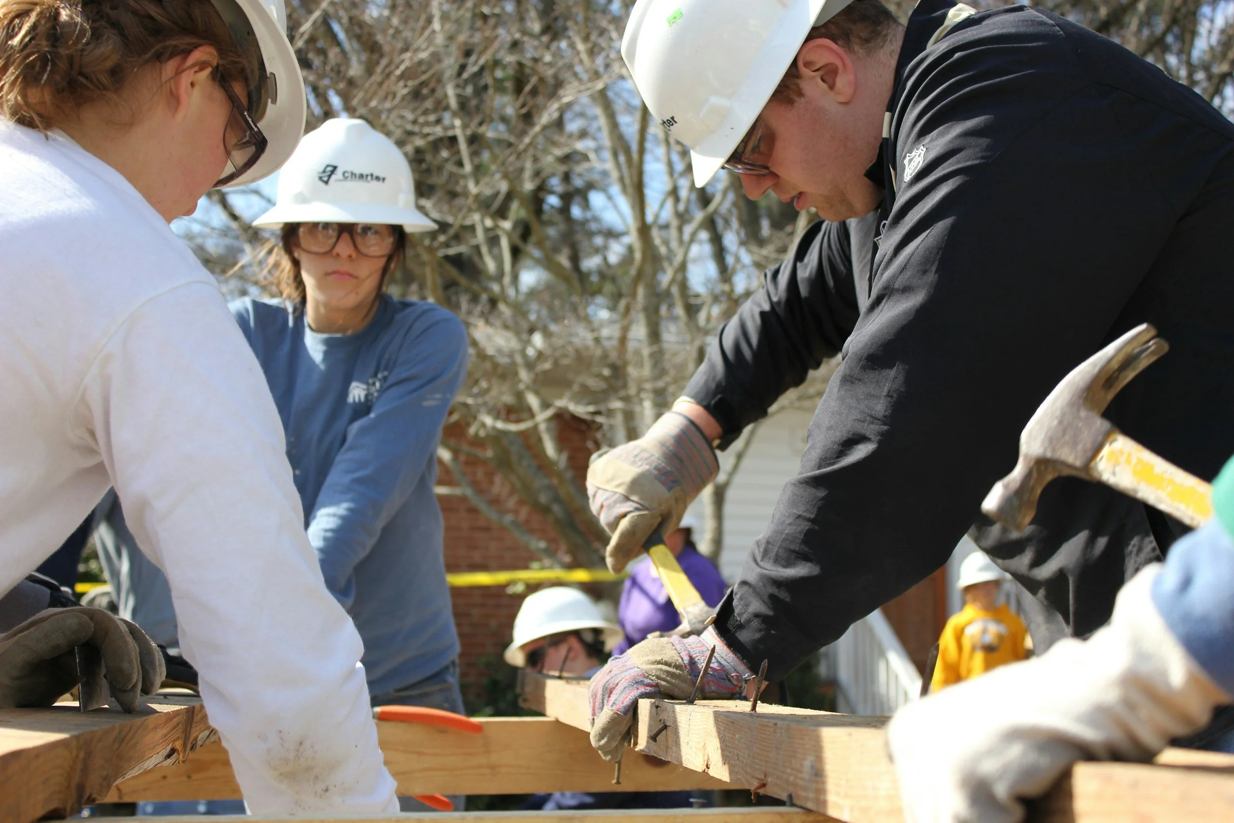 A photo of three people working on a construction site. There is a man holding a hammer and wearing a white hard hat.