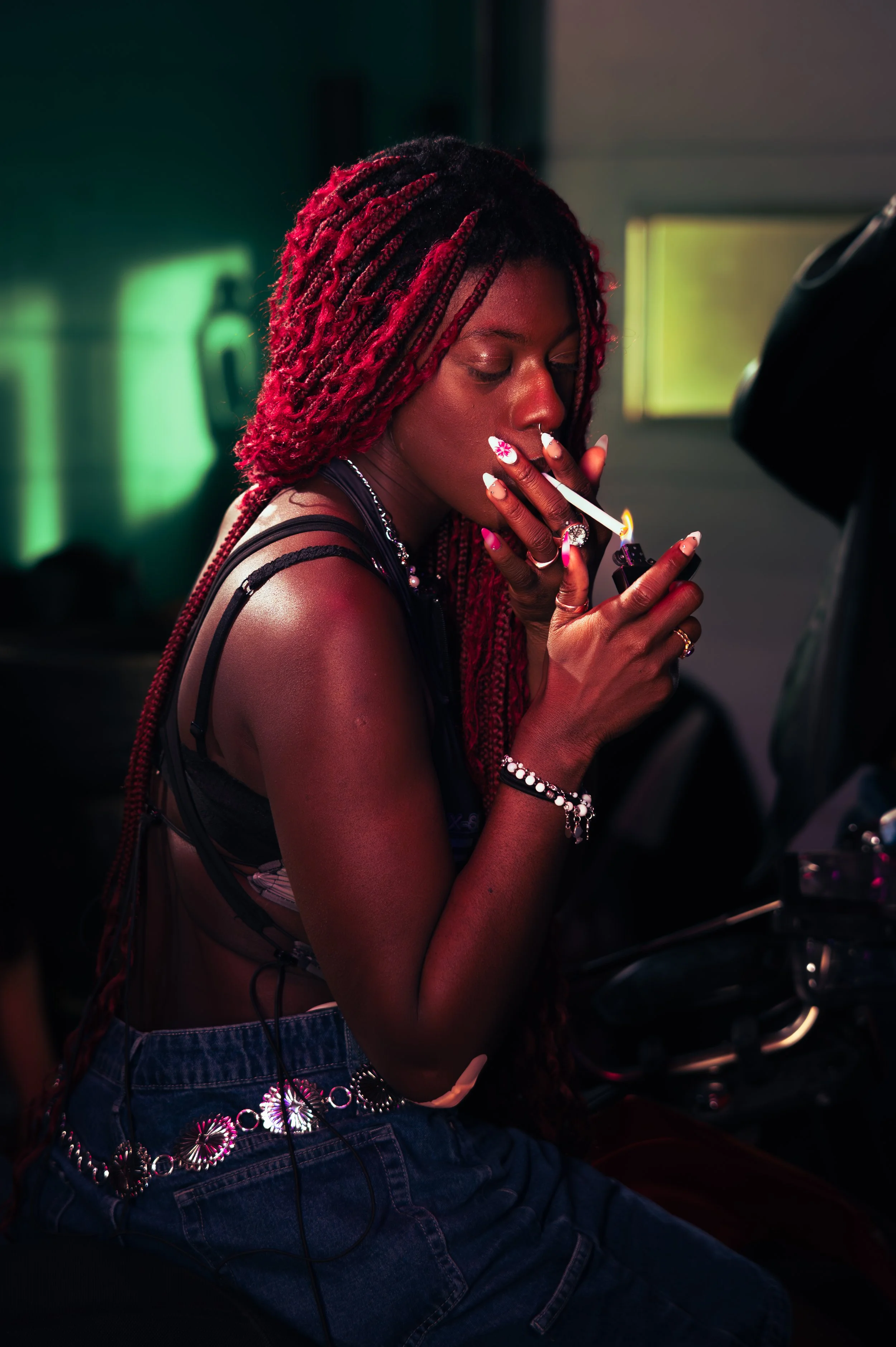 A woman with red dreadlocks lighting a cigarette with a lighter.