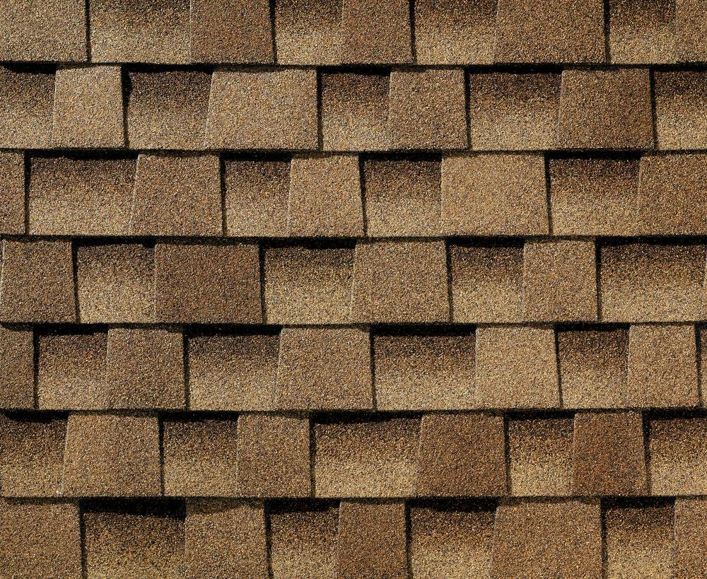 A close-up of a roof with brown asphalt shingles arranged in overlapping rows.