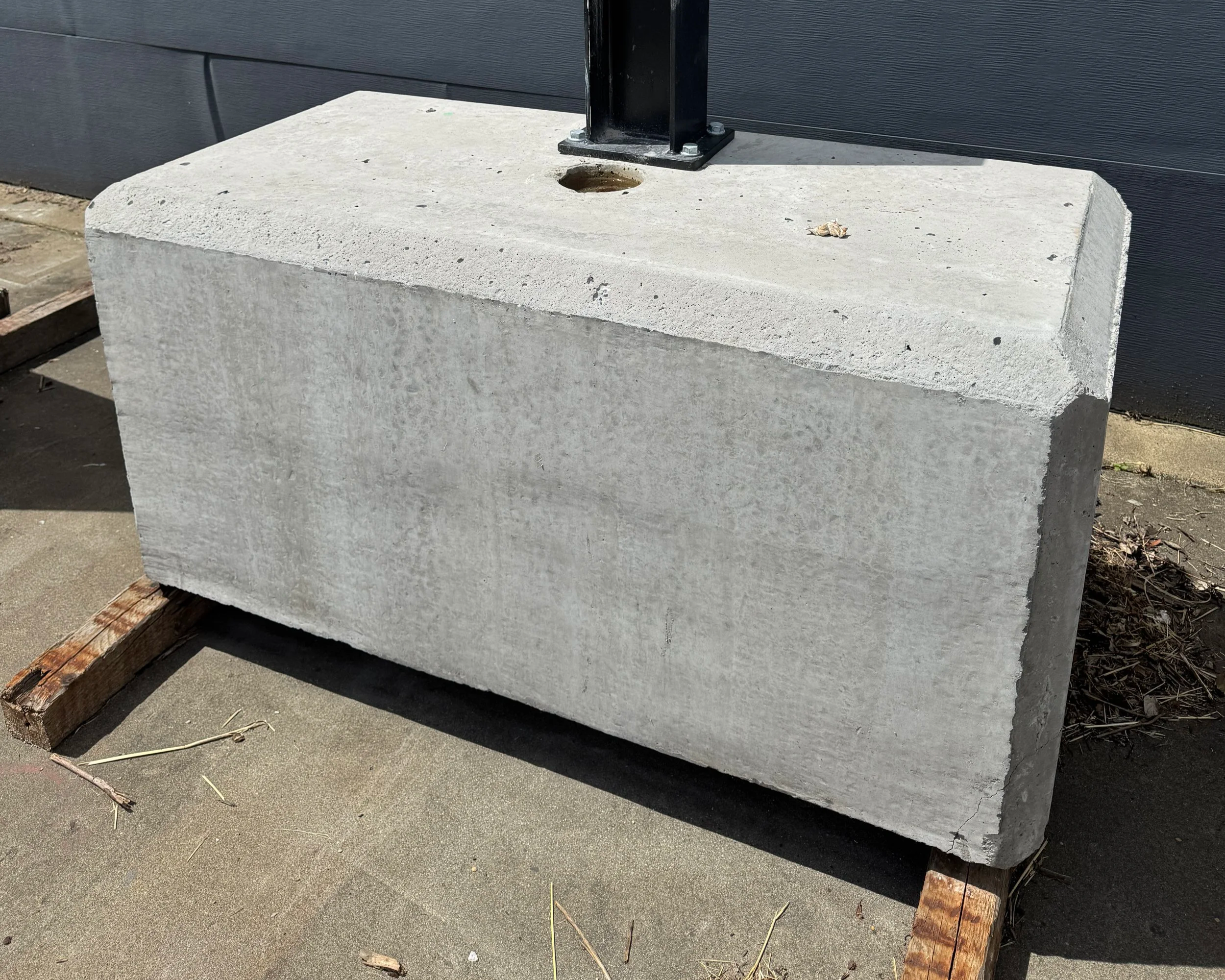 Precast concrete interlocking block with a metal post on top, supported by two wooden planks underneath.