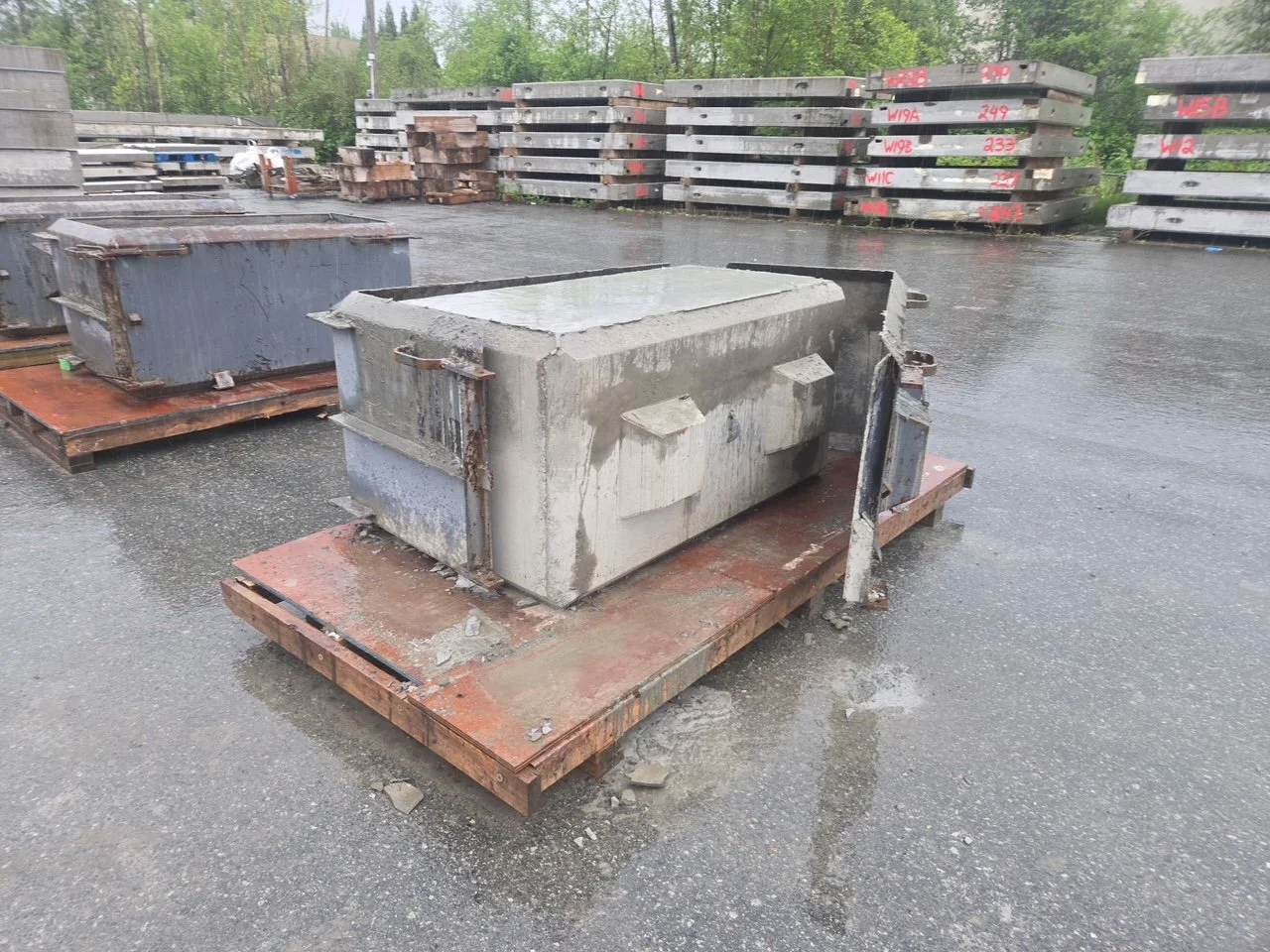 A precast concrete block with the pouring mold around some parts of it, with precast wall panels stacked in the background of the warehouse yard.