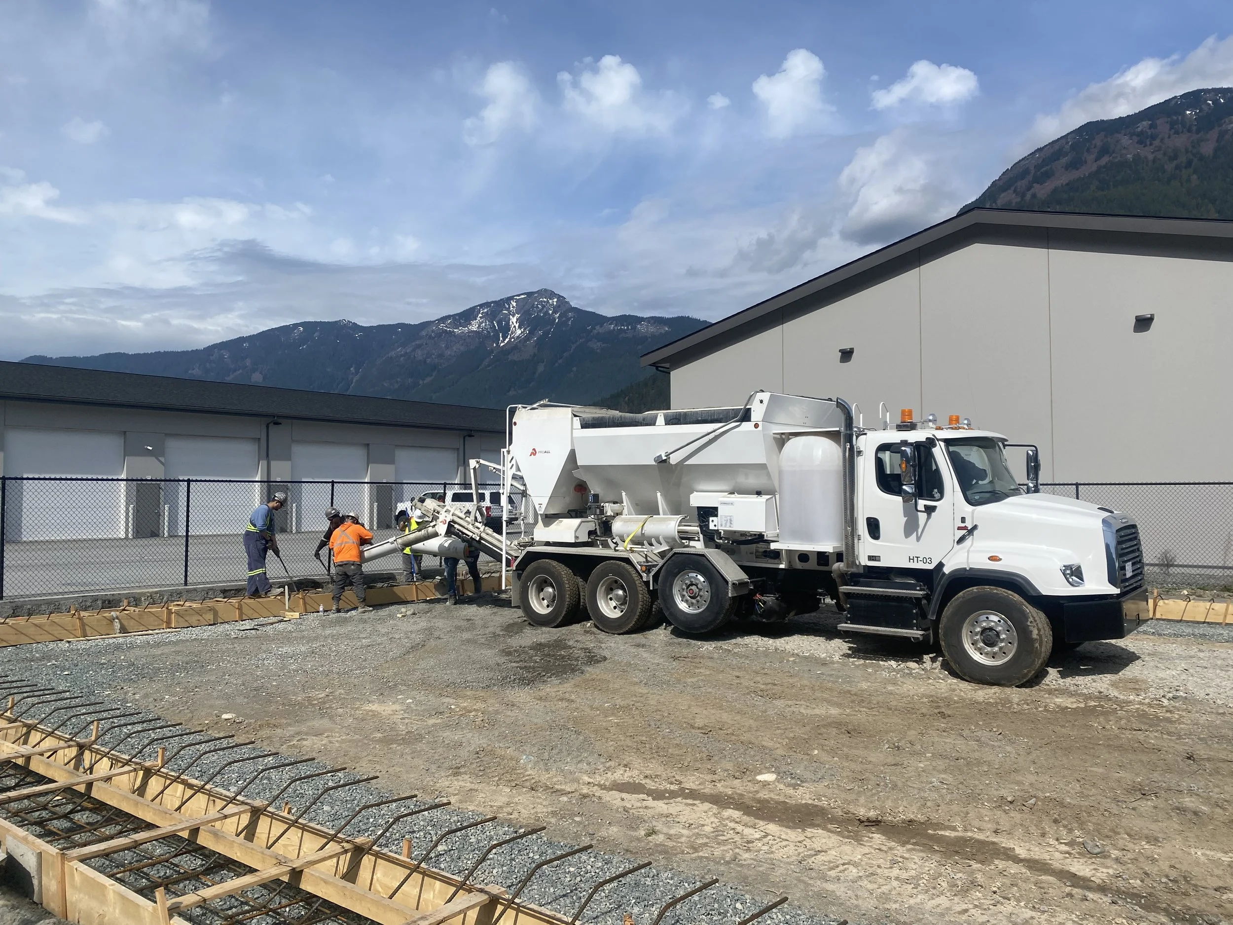 Construction workers pouring concrete on a construction site in Hope, BC,  with mountains and a partly cloudy sky in the background.