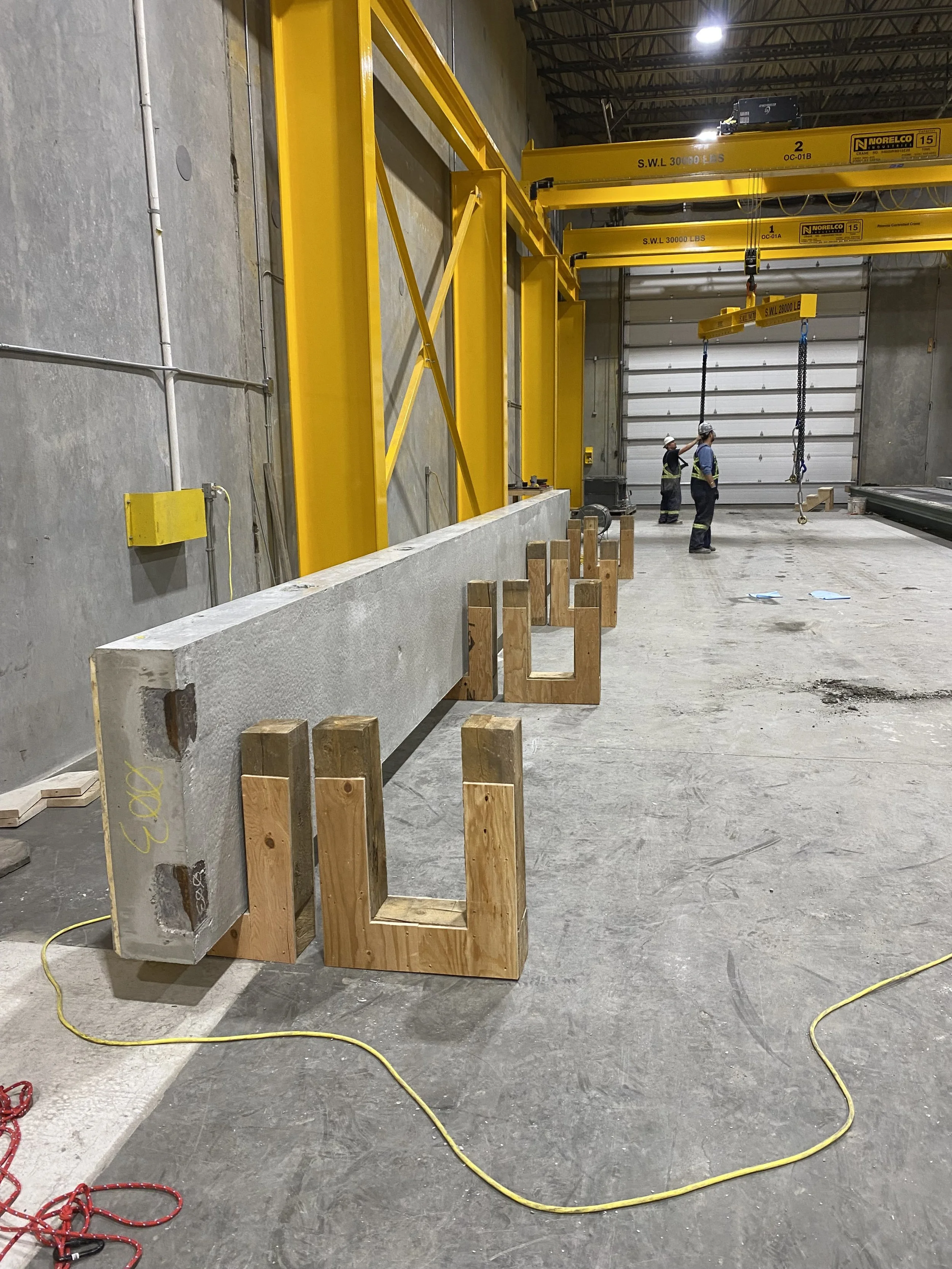Large concrete wall panels lay sideways on the ground in wooden racks inside a precast concrete manufacturing warehouse in Langley.