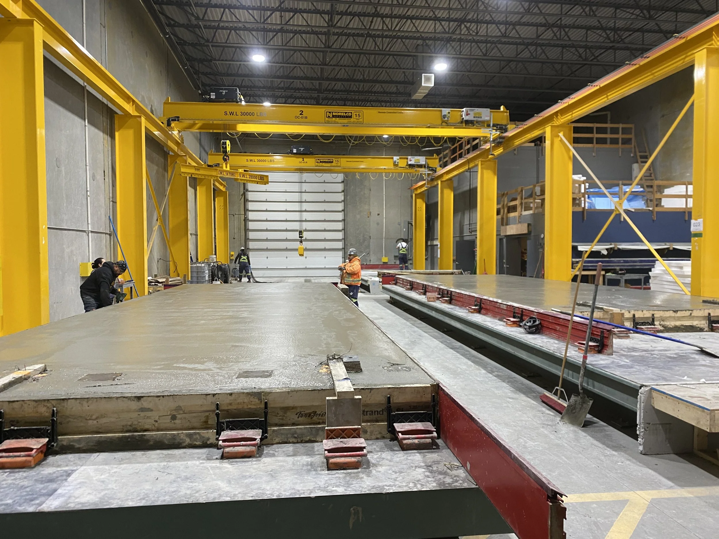 Recently poured precast concrete panels inside an industrial warehouse in Langley, BC, with yellow overhead cranes and large concrete slabs.